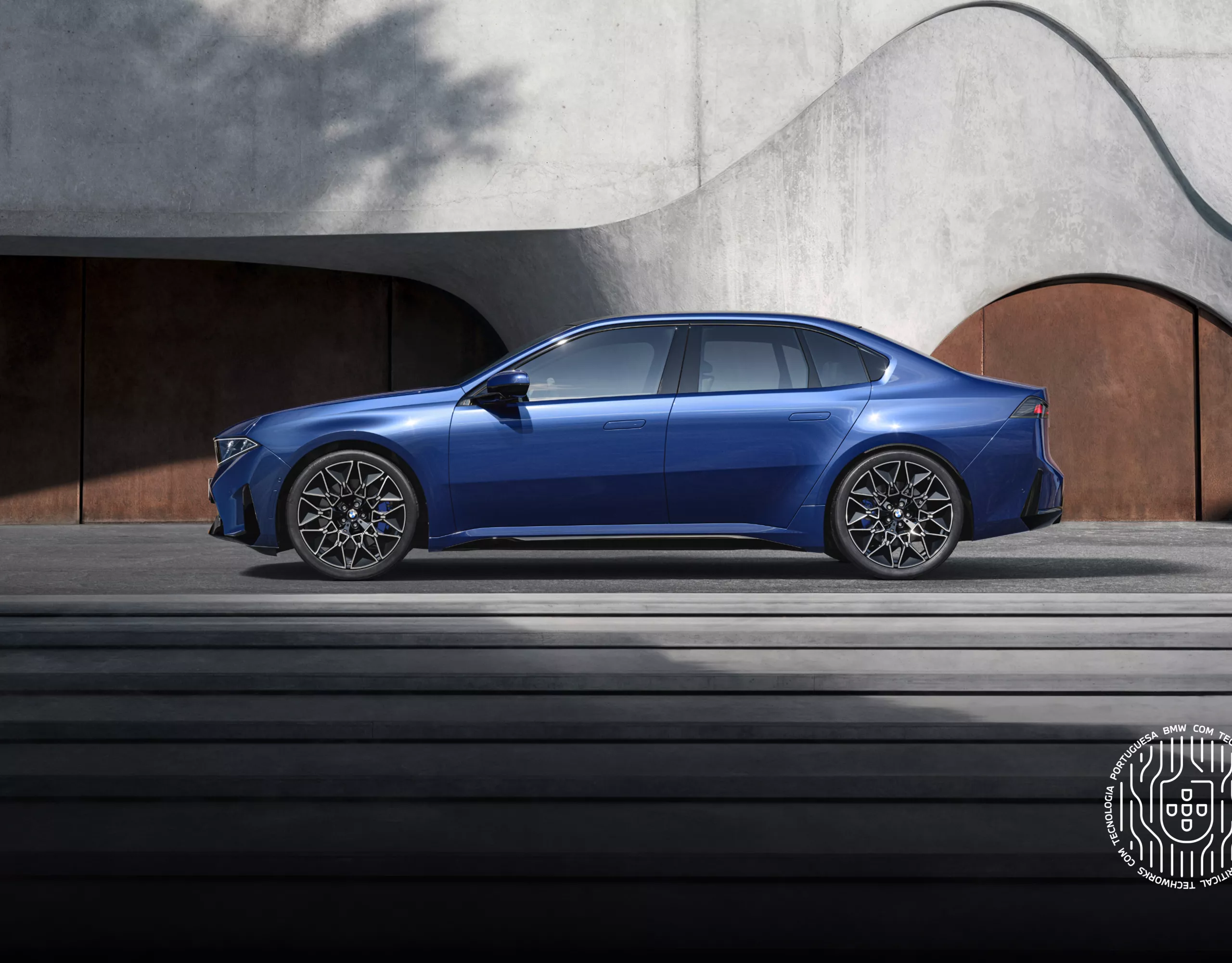 BMW i3 visto de lado, estacionado junto a um edifício de betão com escadas em  primeiro plano.