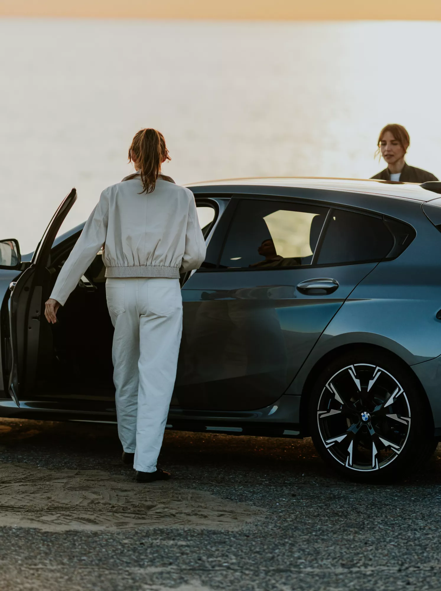 Grauer BMW 1er fährt bei Sonnenlicht auf einer Küstenstraße und präsentiert sportliches Design, moderne Frontansicht und dynamische Fahreigenschaften.