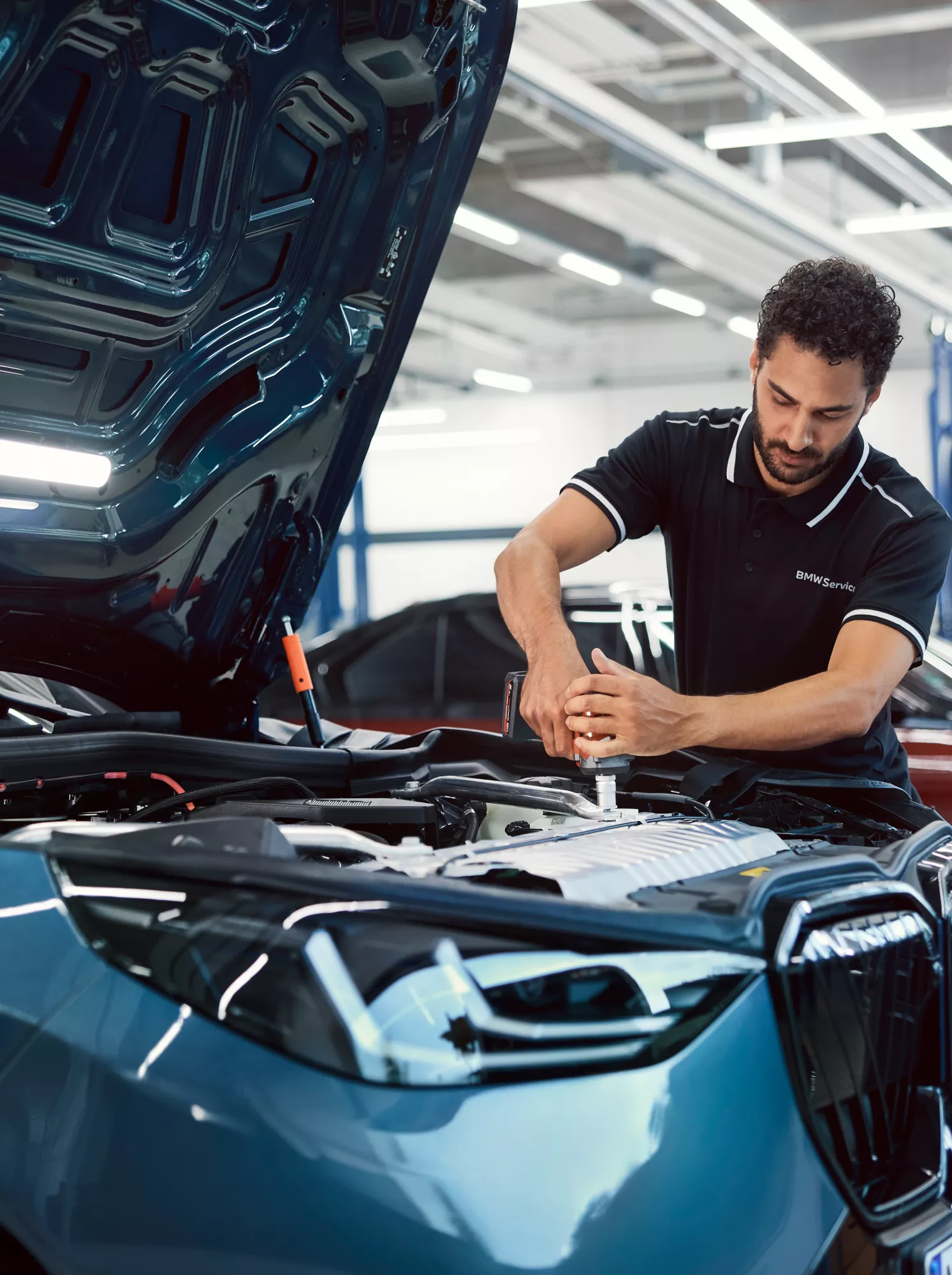 Técnico BMW Service a trabalhar no motor de um BMW azul com o capô aberto, dentro de uma oficina.