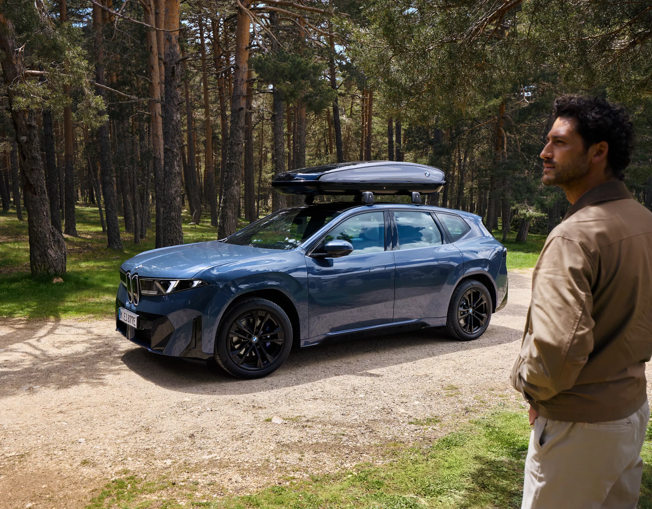 Deux personnes se tiennent devant une BMW iX3 avec un coffre de toit et regardent au loin