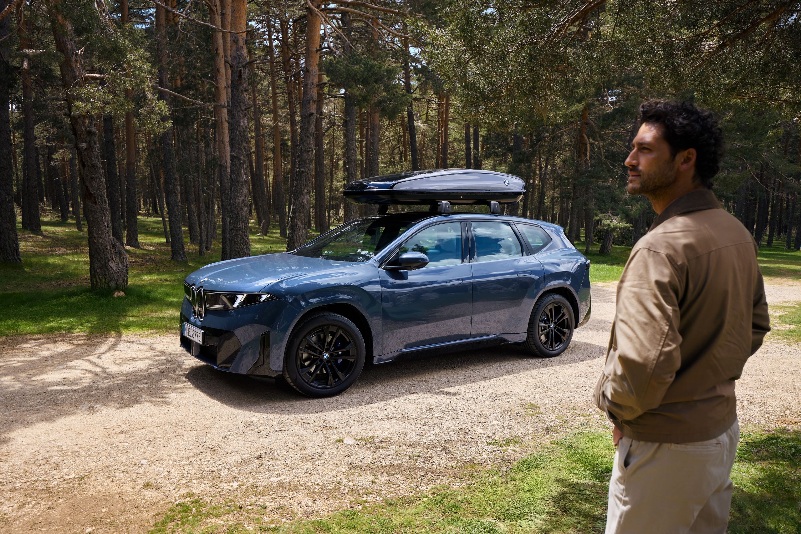 Deux personnes se tiennent devant une BMW iX3 avec un coffre de toit et regardent au loin