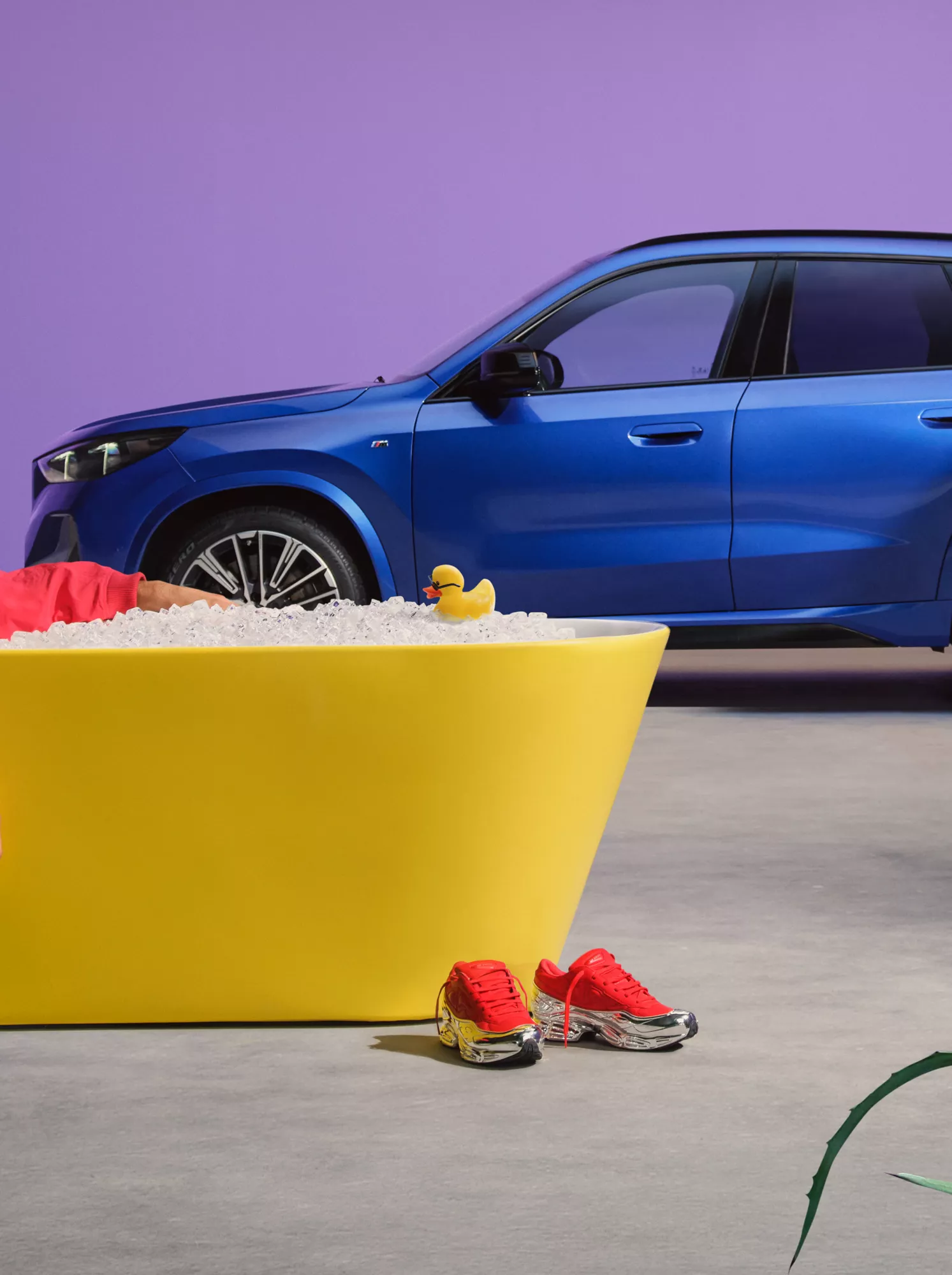 Mężczyzna siedzący w wannie z kostkami lodu, w tle niebieski samochód BMW.