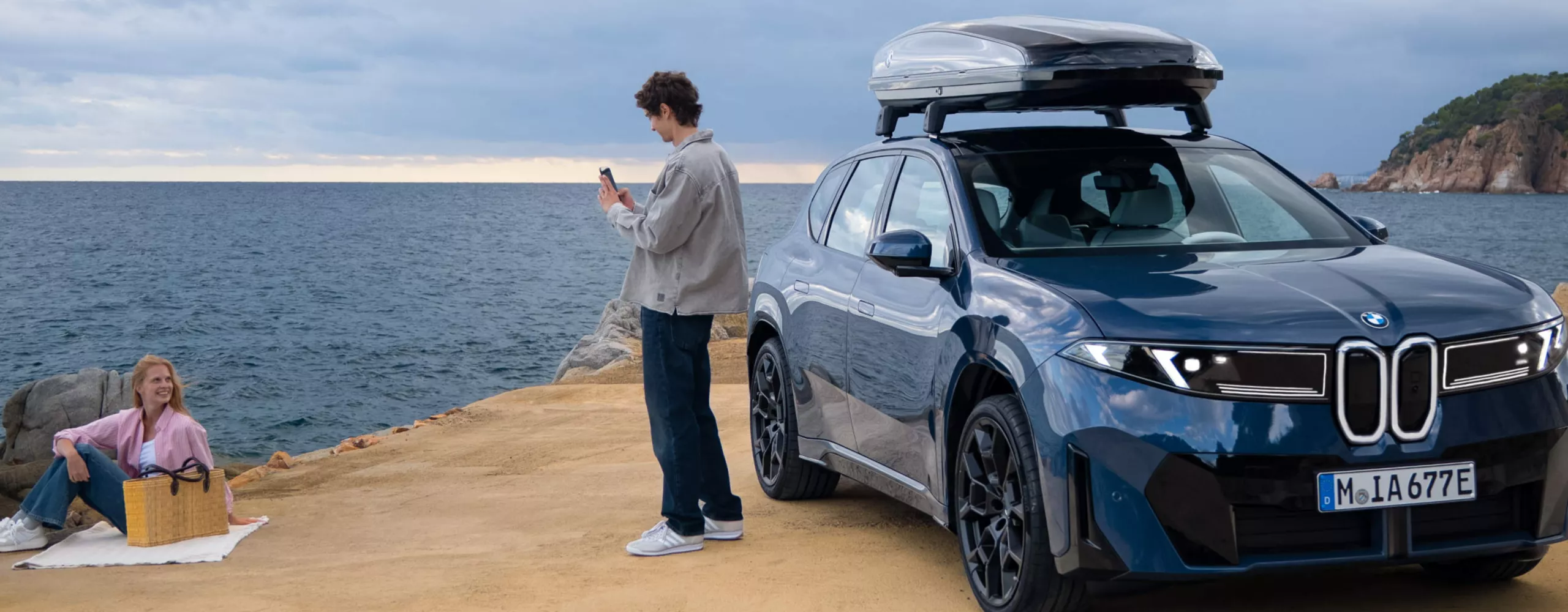 Mies pysäköid taken BMW iX3:n vieressä meren rannalla