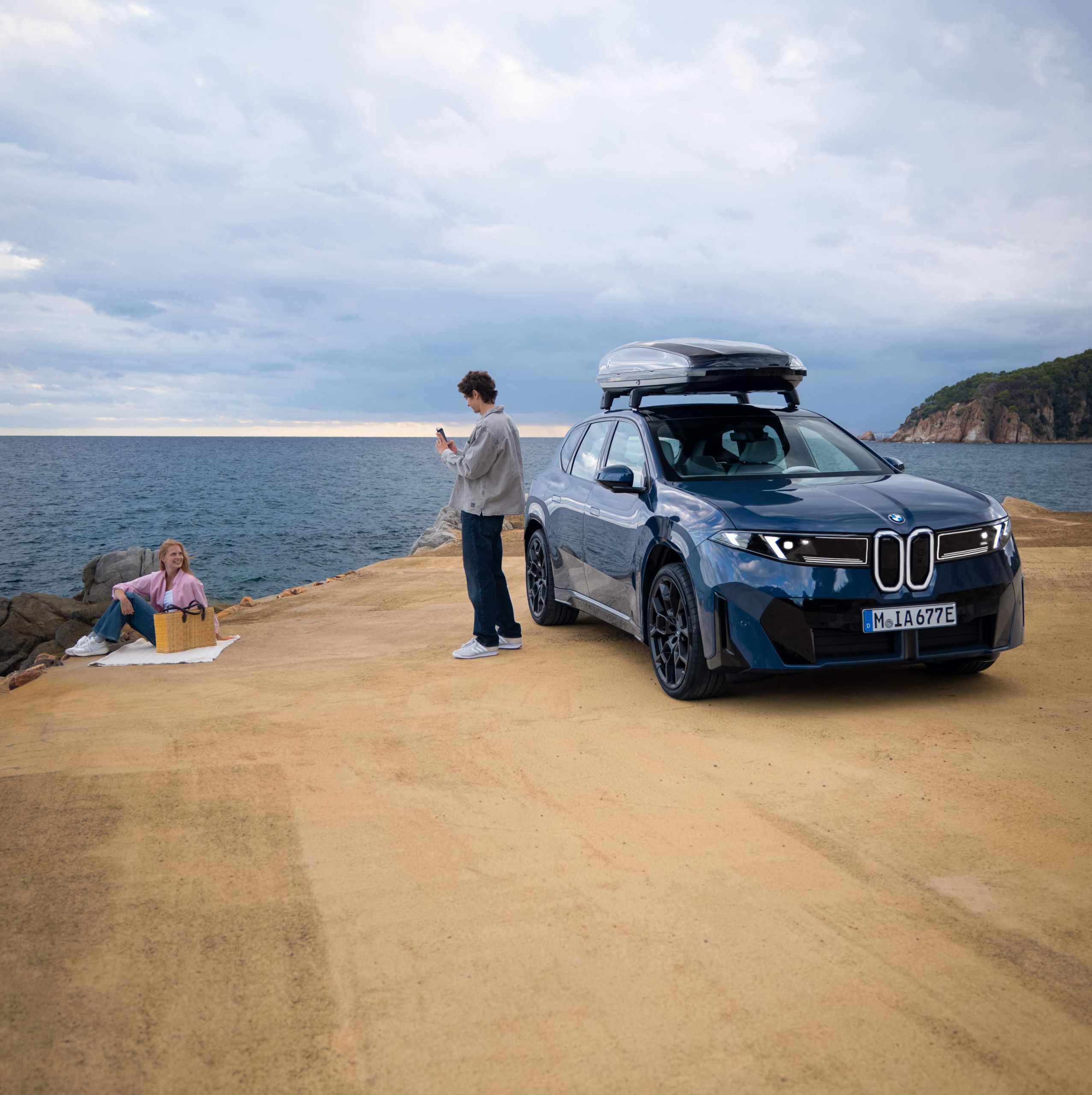 Man bredvid en parkerad BMW iX3 vid havet