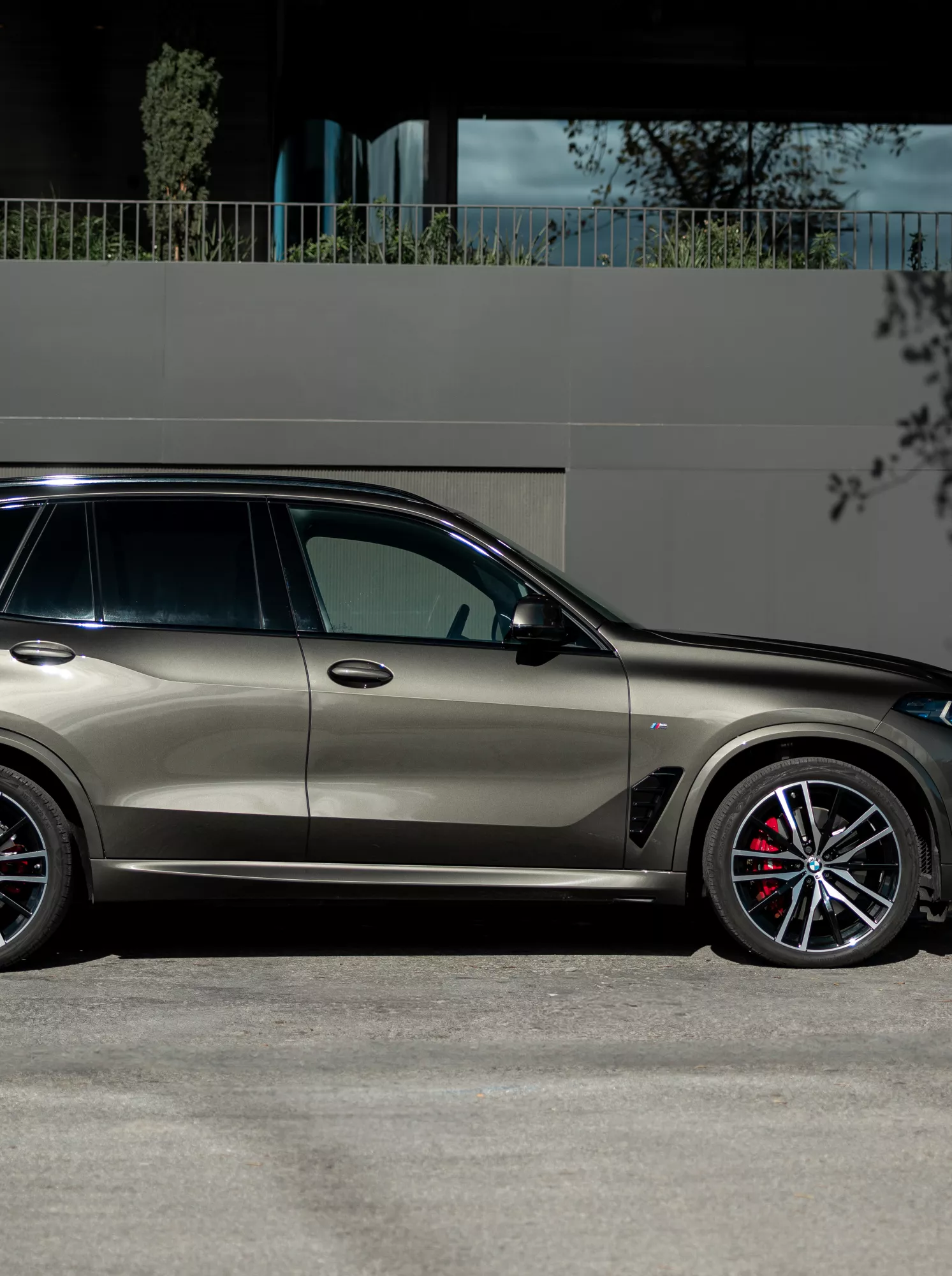 A BMW X5 egy utcán parkol egy fal mellett, mellette egy személy