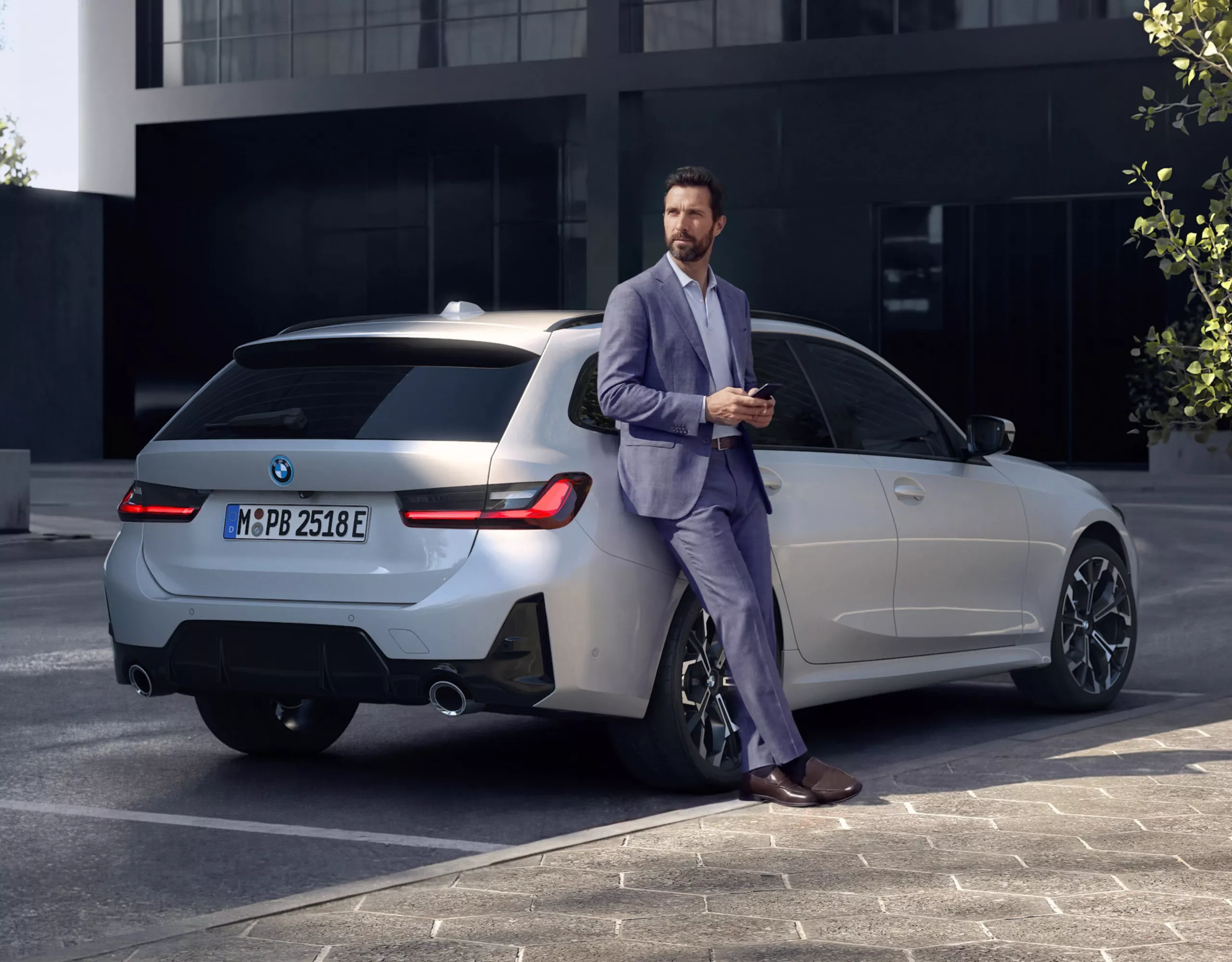 Person lehnt an silbernem BMW Touring vor modernem Gebäude in urbaner Umgebung