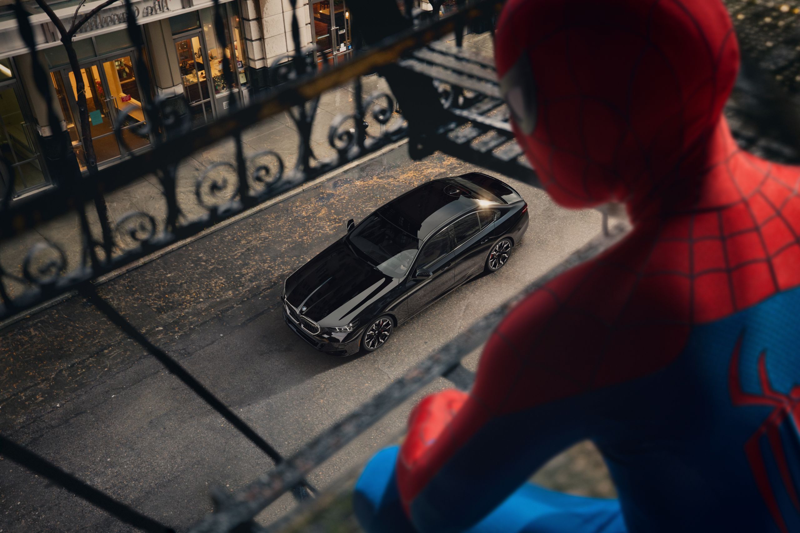 An over-the-shoulder shot of Spider-Men looking down on a BMW 5 Series from a fire escape.