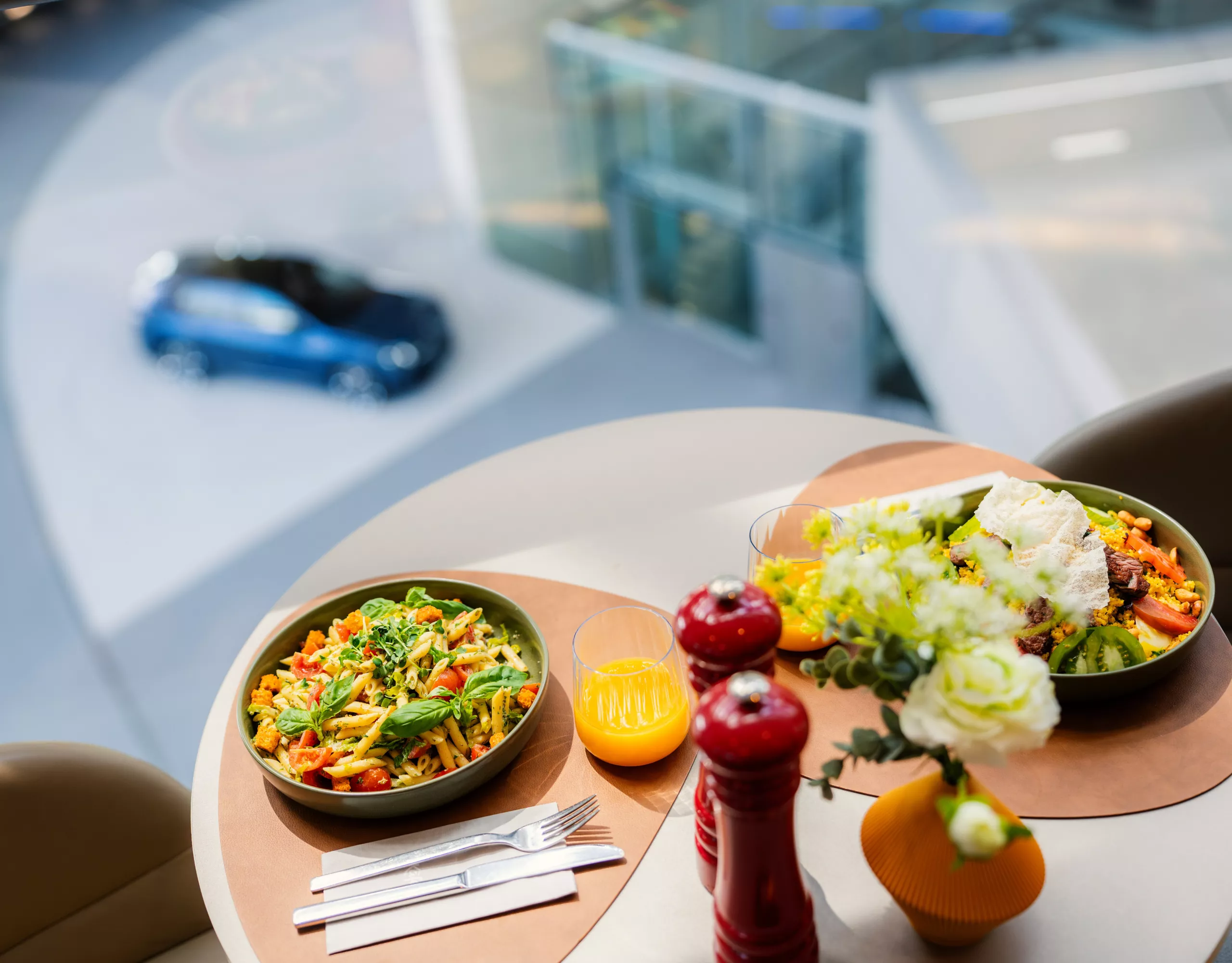 Set table with fresh dishes and drinks in BMW Welt Premium Lounge, with a displayed vehicle visible in the background.