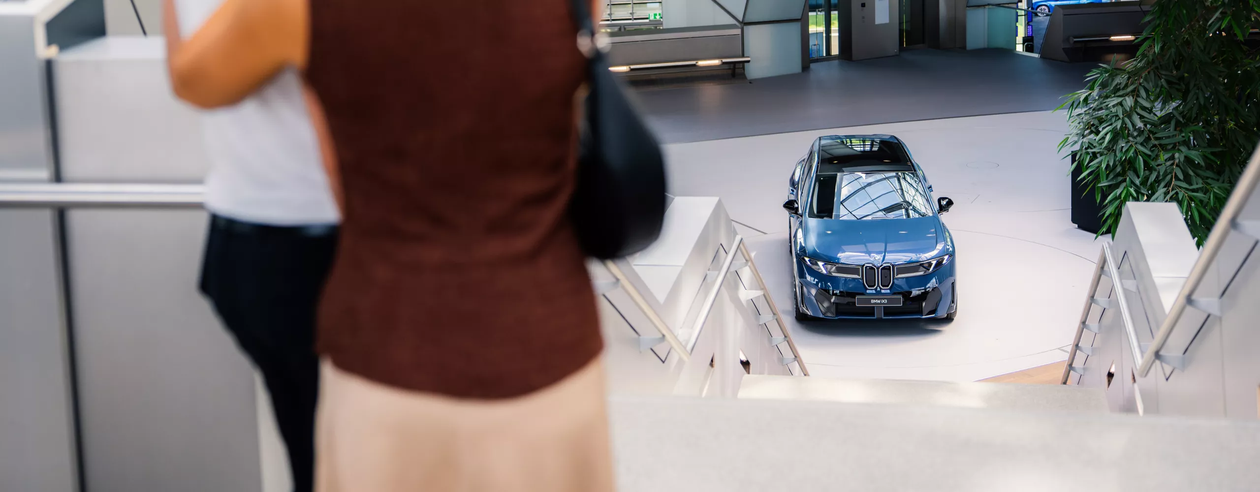 An adult couple walks together towards a BMW iX3 at BMW Welt.