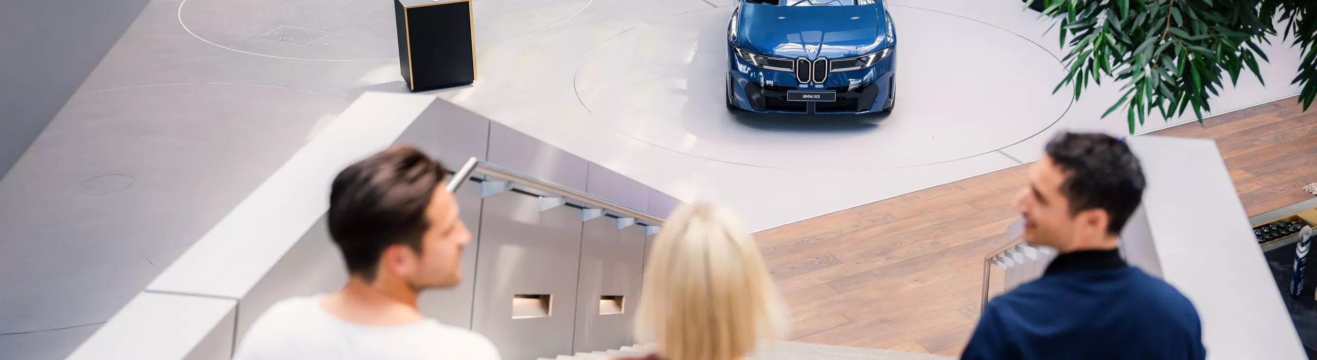 An adult couple walks down the stairs at BMW Welt, looking at a displayed BMW iX3.