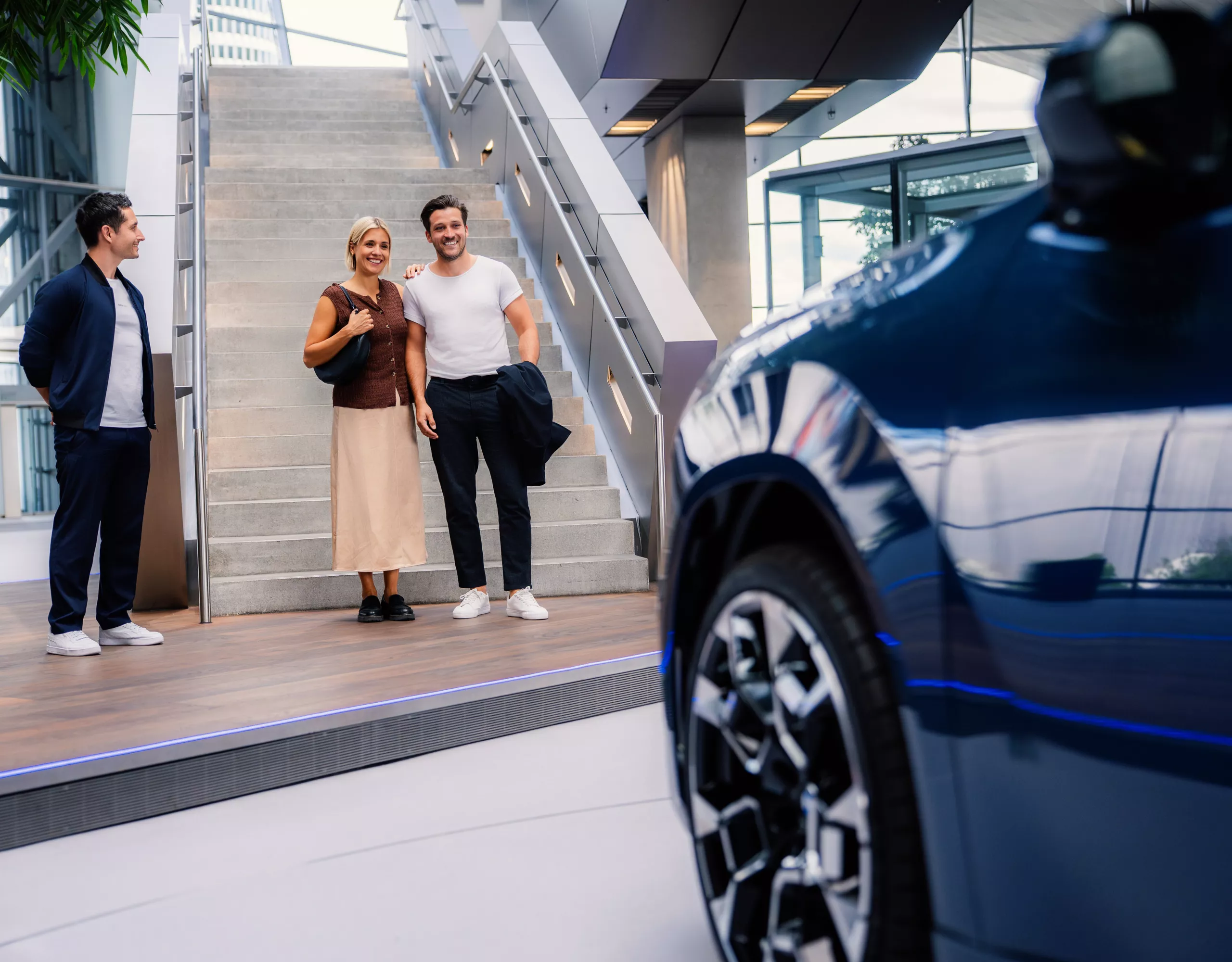 An adult couple walks down stairs at BMW Welt towards a BMW iX3.
