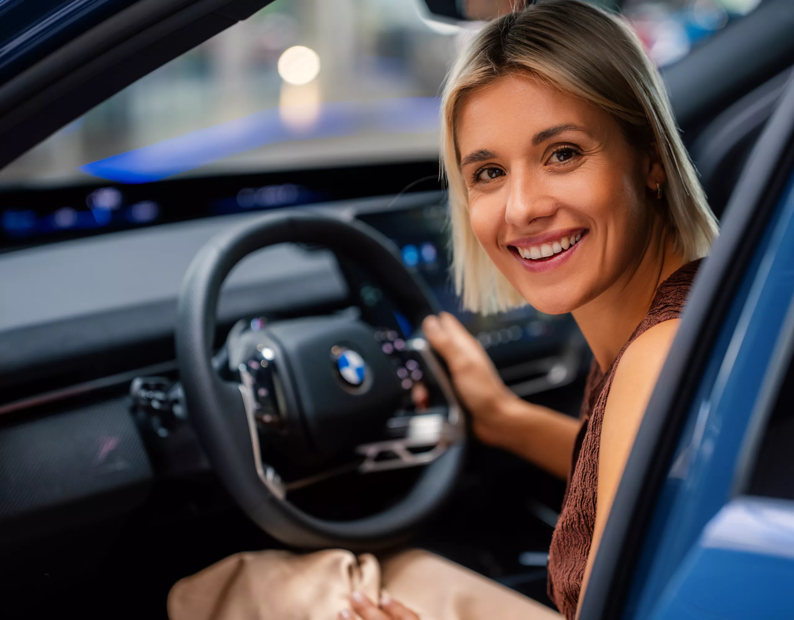 A woman sits in the driver’s seat of the BMW iX3, using the steering wheel inside the vehicle.