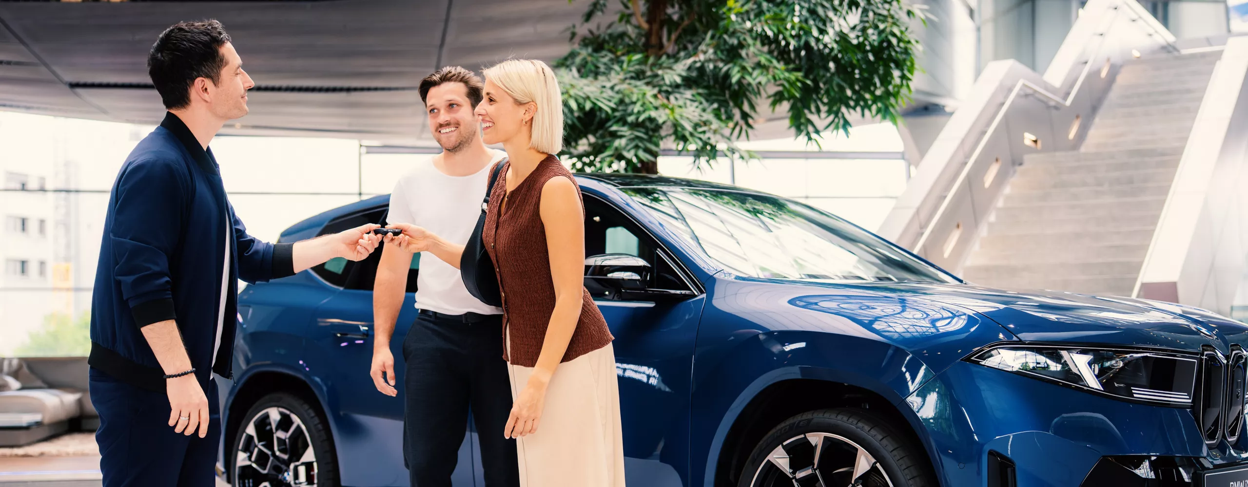 An adult couple receives the keys for the BMW iX3 from a staff member at BMW Welt.