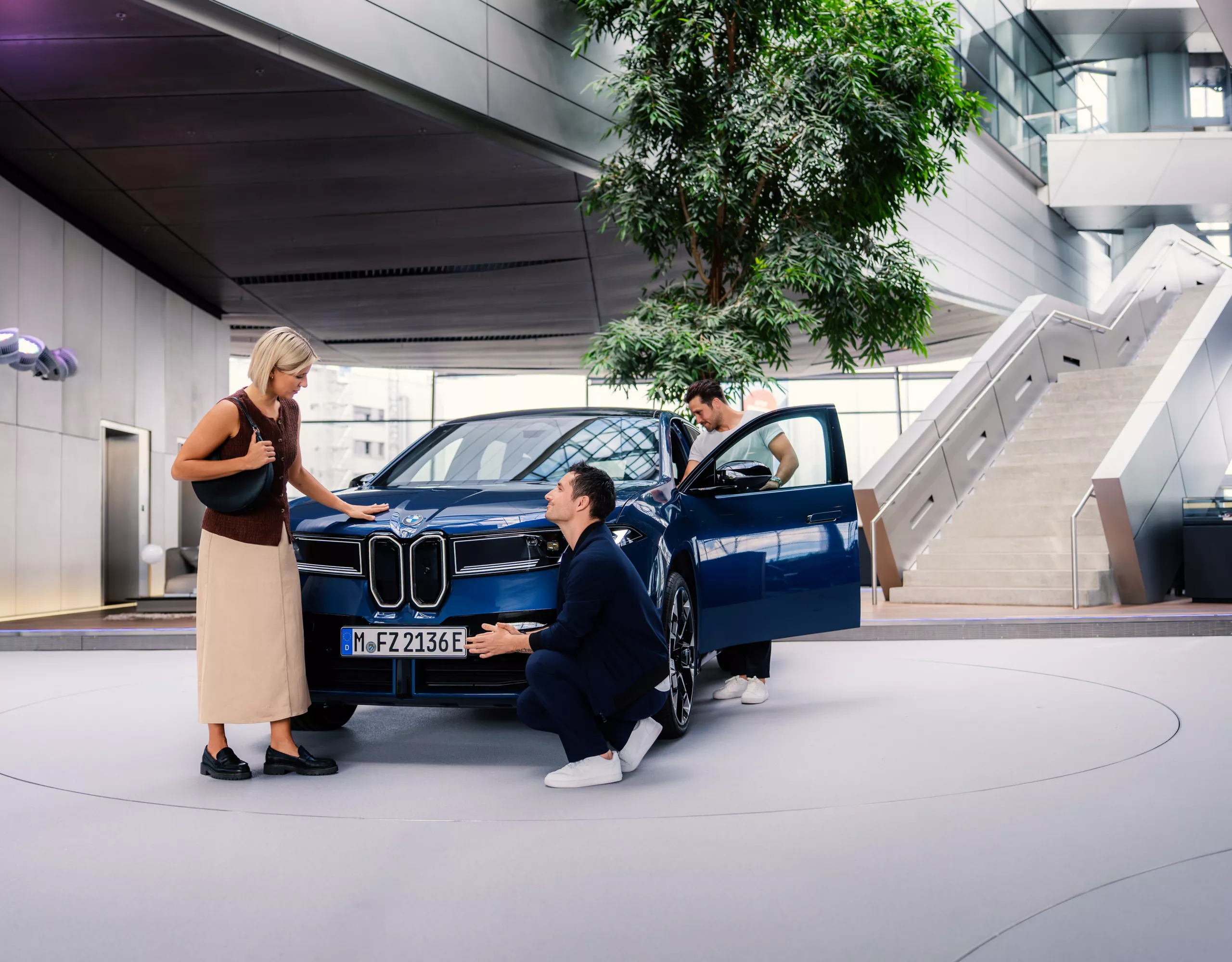 An adult couple explores the BMW iX3 at BMW Welt while a staff member presents the vehicle in detail.