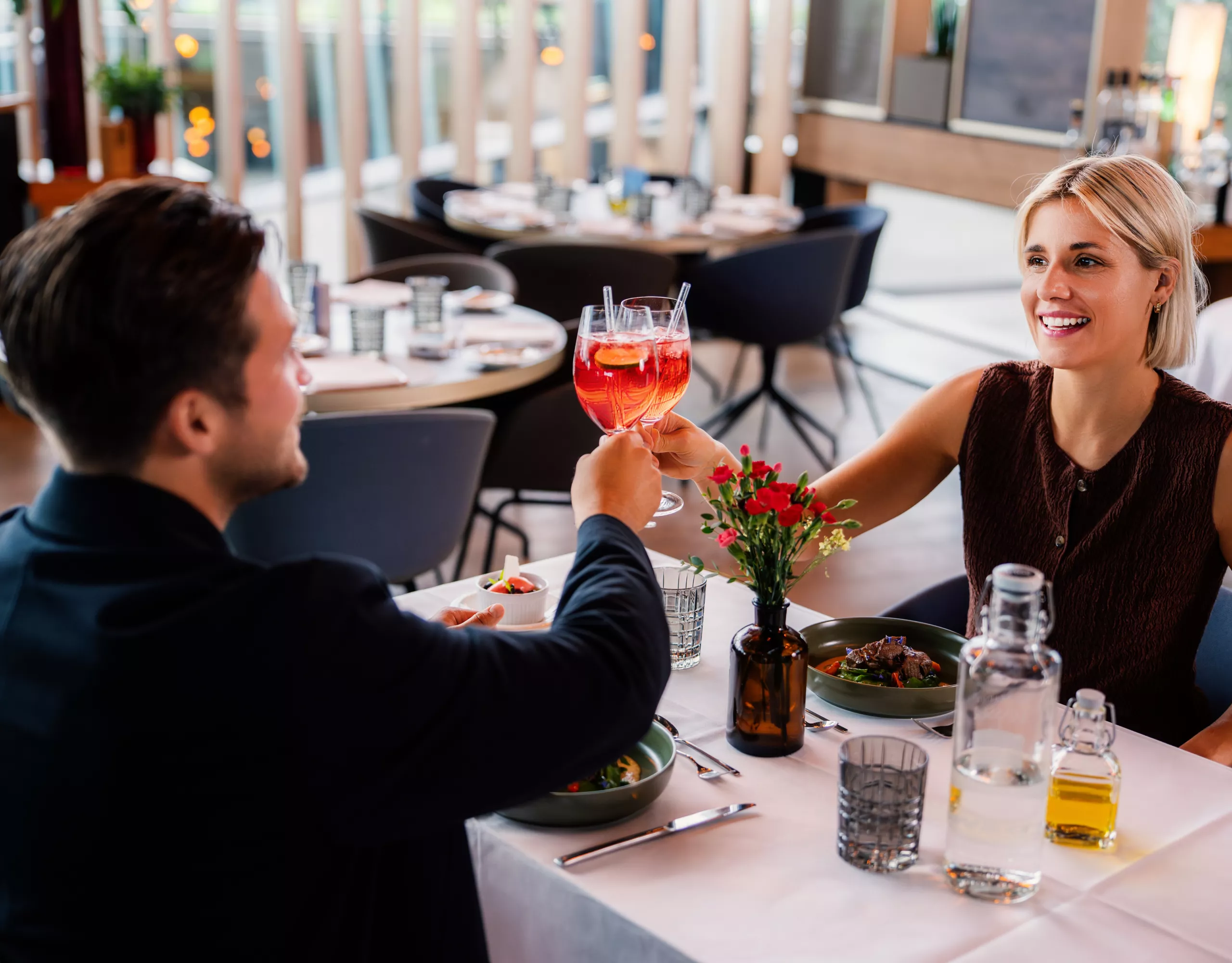 An adult couple enjoys dinner at the Bavarie by Käfer at BMW Welt dining, toasting together.