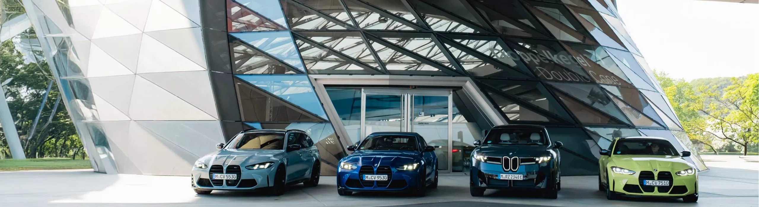 Four BMW vehicles positioned in front of the Double Cone at BMW Welt in Munich.