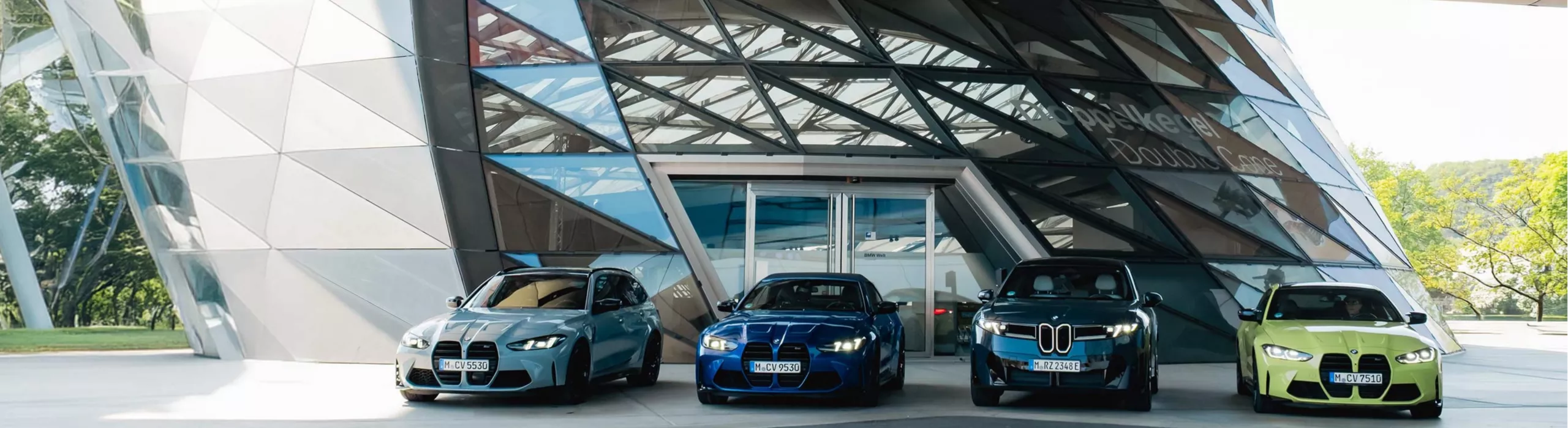 Vier BMW Fahrzeuge vor dem Doppelkegel der BMW Welt in München.