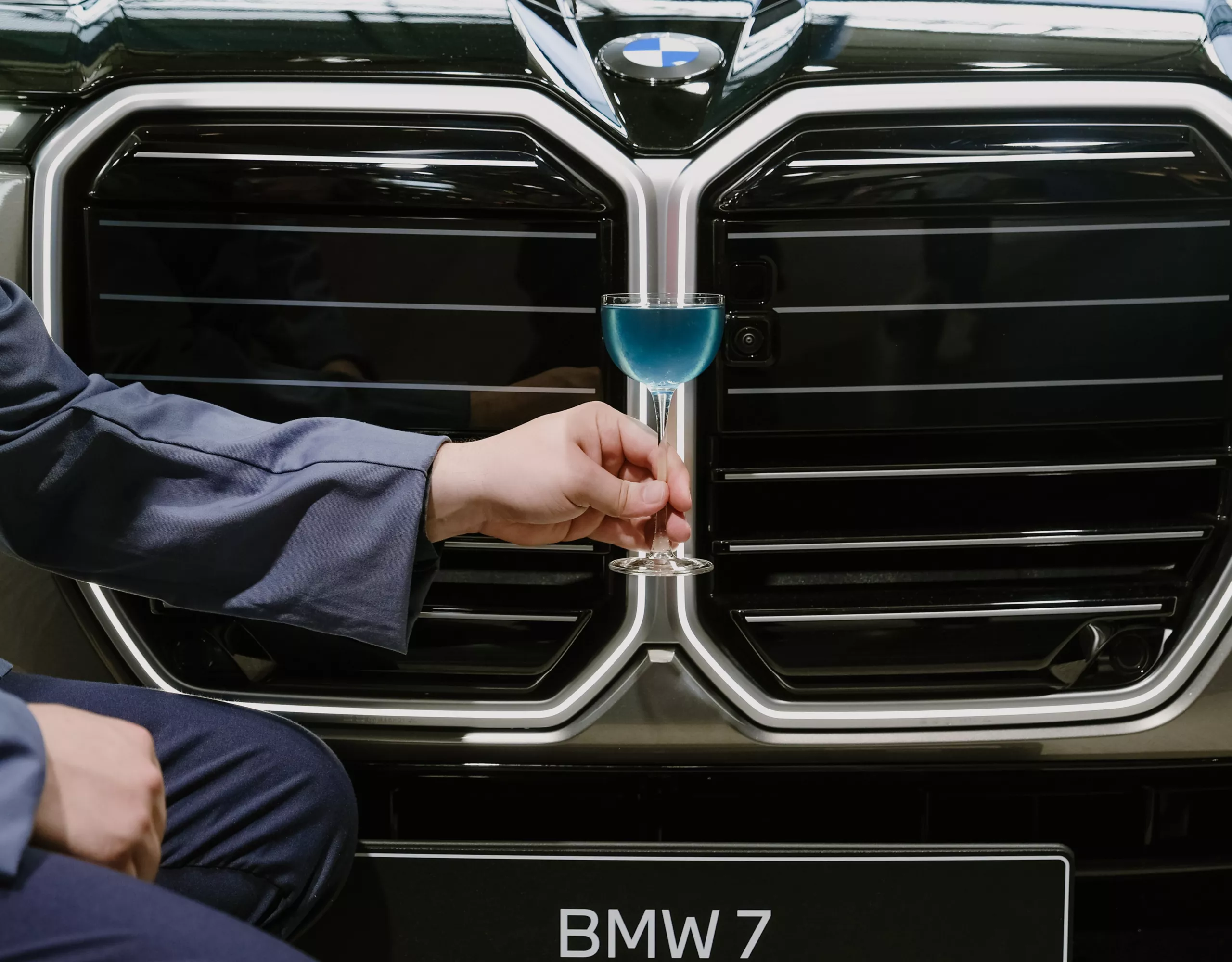 Blue cocktail held in front of the illuminated BMW kidney grille of a BMW 7 at BMW Welt.