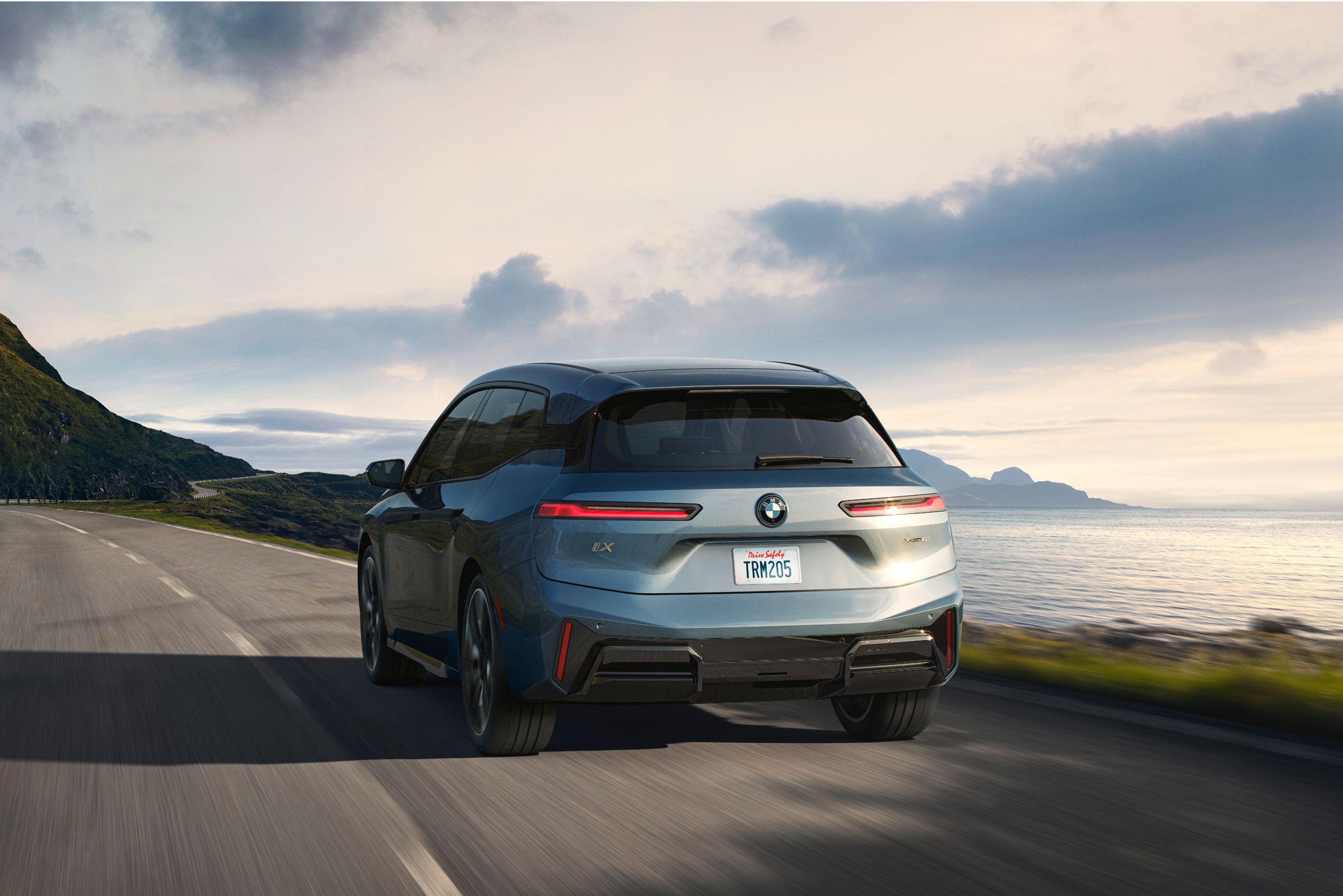 A rear shot of the BMW iX as it drives down a costal highway