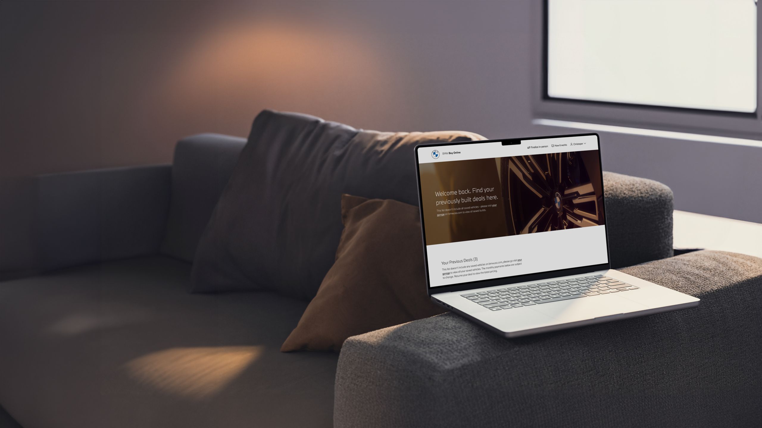 A laptop perched on the arm of a loveseat, with the screen showing the BMW Buy Online experience.