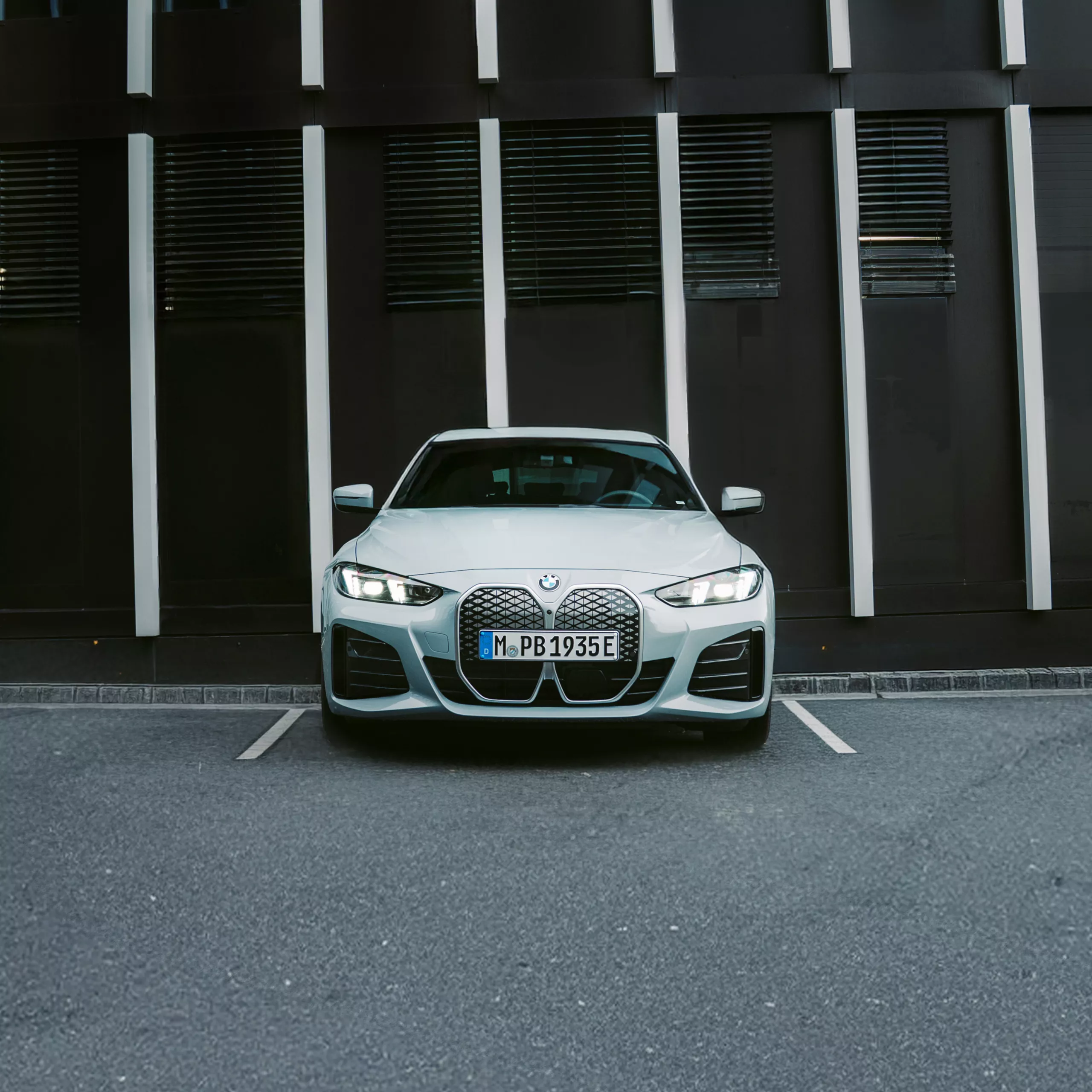 En BMW i4 står parkerad på en parkeringsplats framför en byggnad med fronten mot kameran