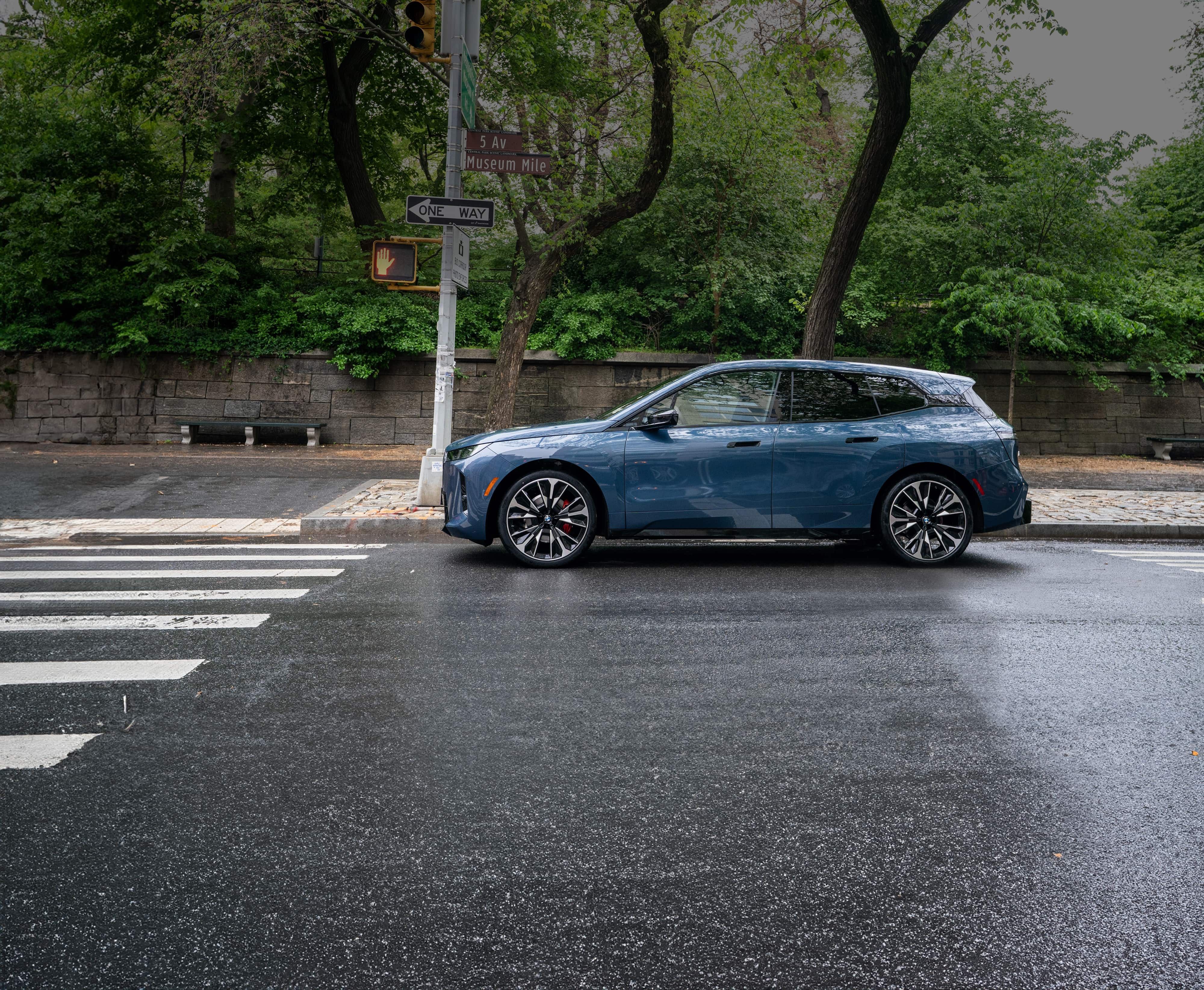 A side profile shot of the BMW iX parked on a city street with lush foliage behind it