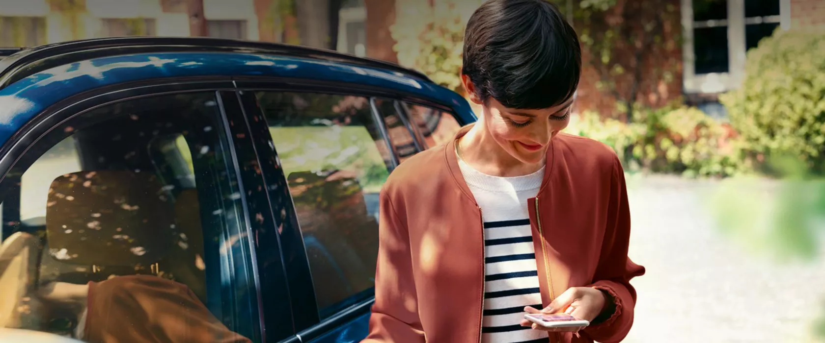 Mulher sorridente a mexer no telemóvel junto do seu BMW.