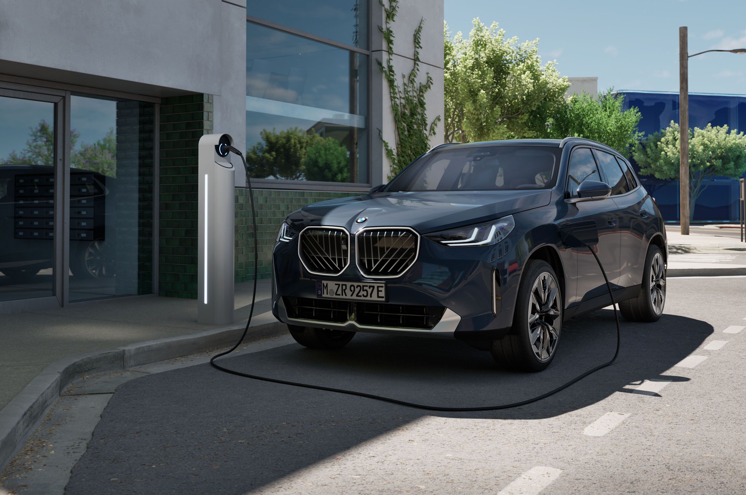 BMW X3 híbrido enchufable cargando en un punto de recarga urbano frente a un edificio moderno