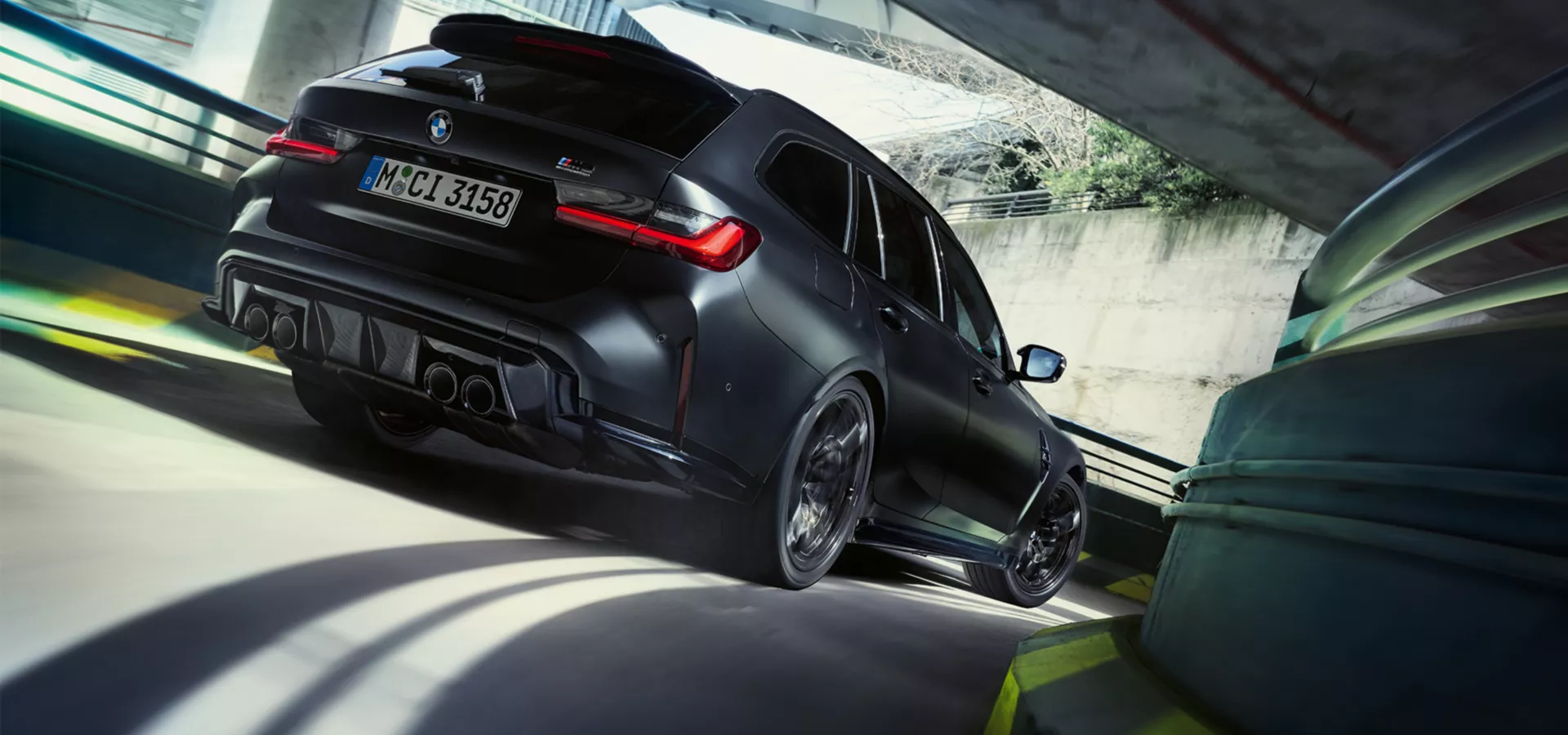 Ein matt schwarzer BMW M3 Touring xDrive fährt eine kurvige Garagenauffahrt hinunter.