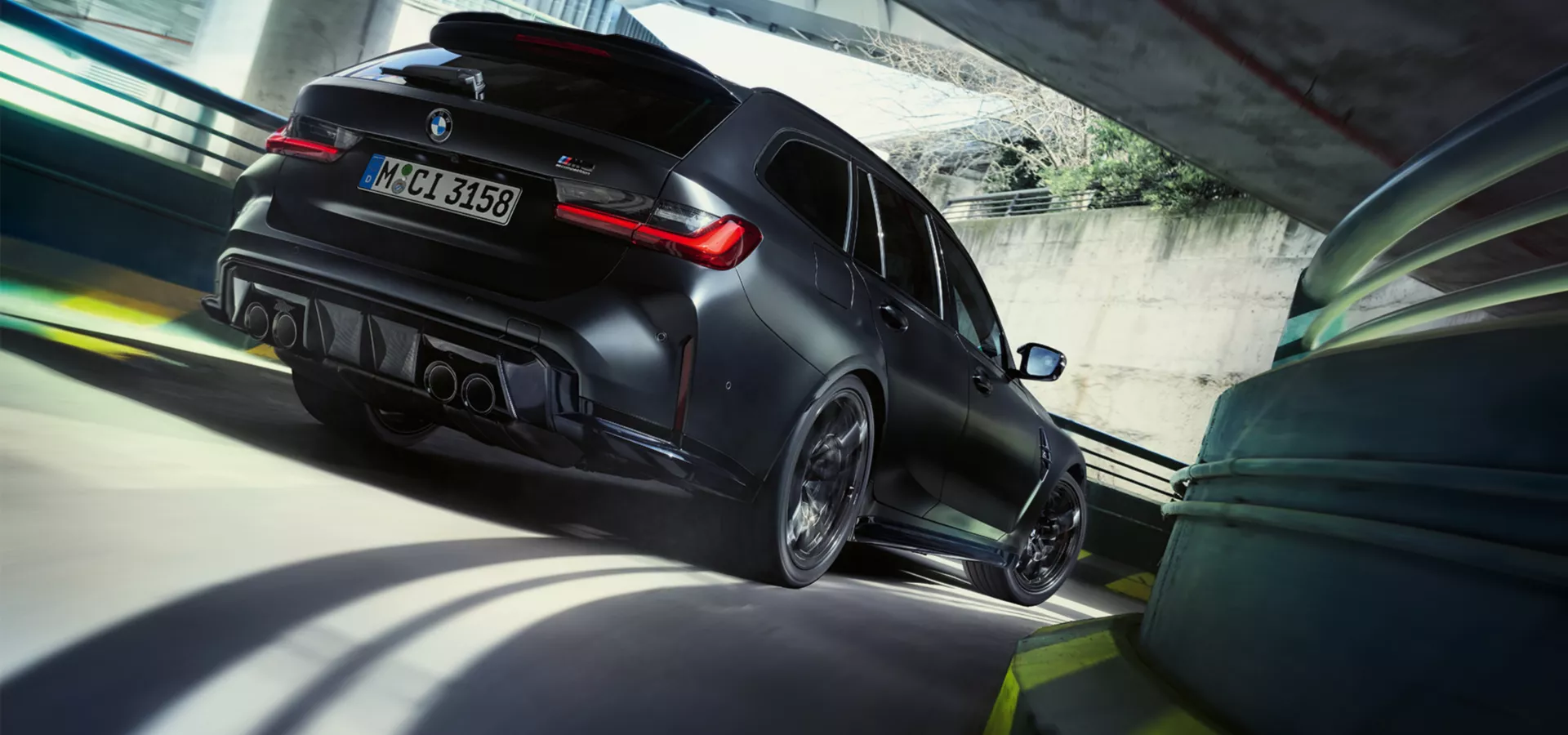 Ein matt schwarzer BMW M3 Touring xDrive fährt eine kurvige Garagenauffahrt hinunter.