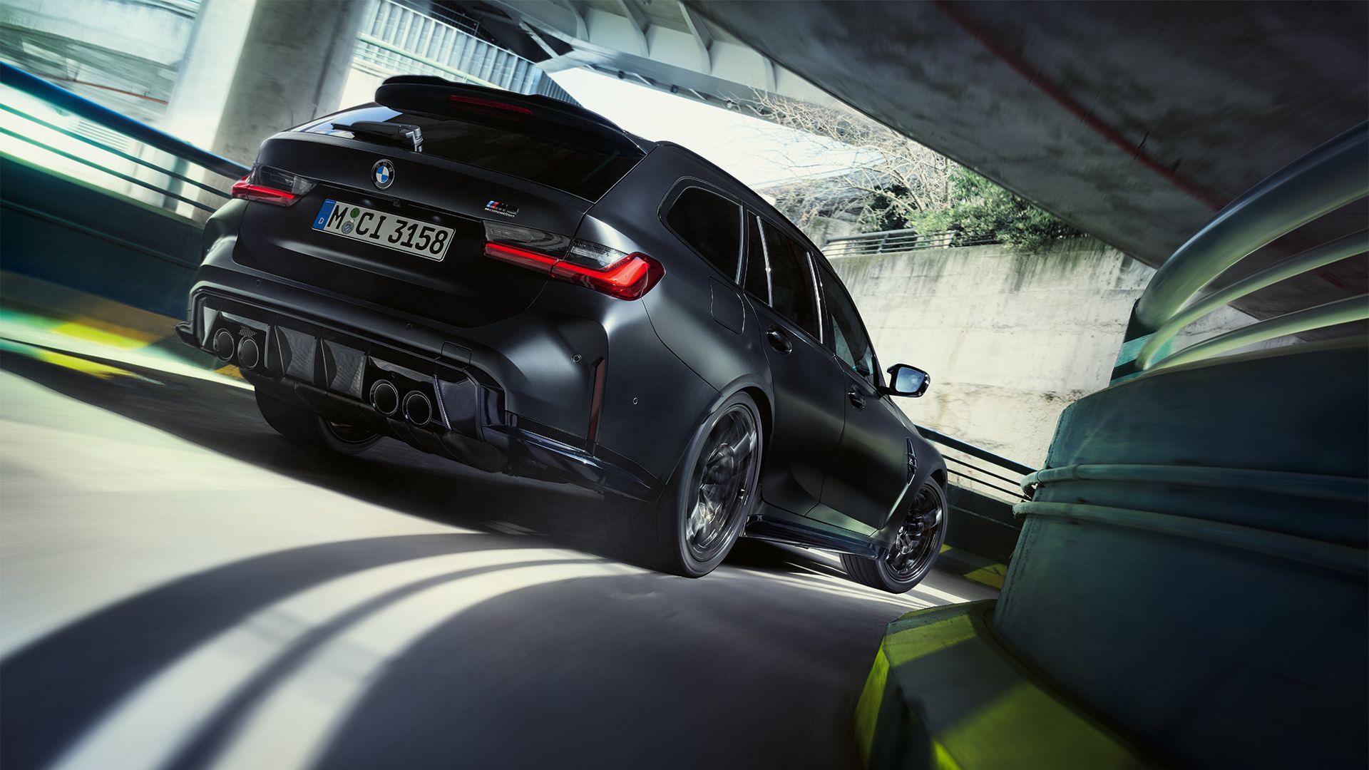 Ein matt schwarzer BMW M3 Touring xDrive fährt eine kurvige Garagenauffahrt hinunter.