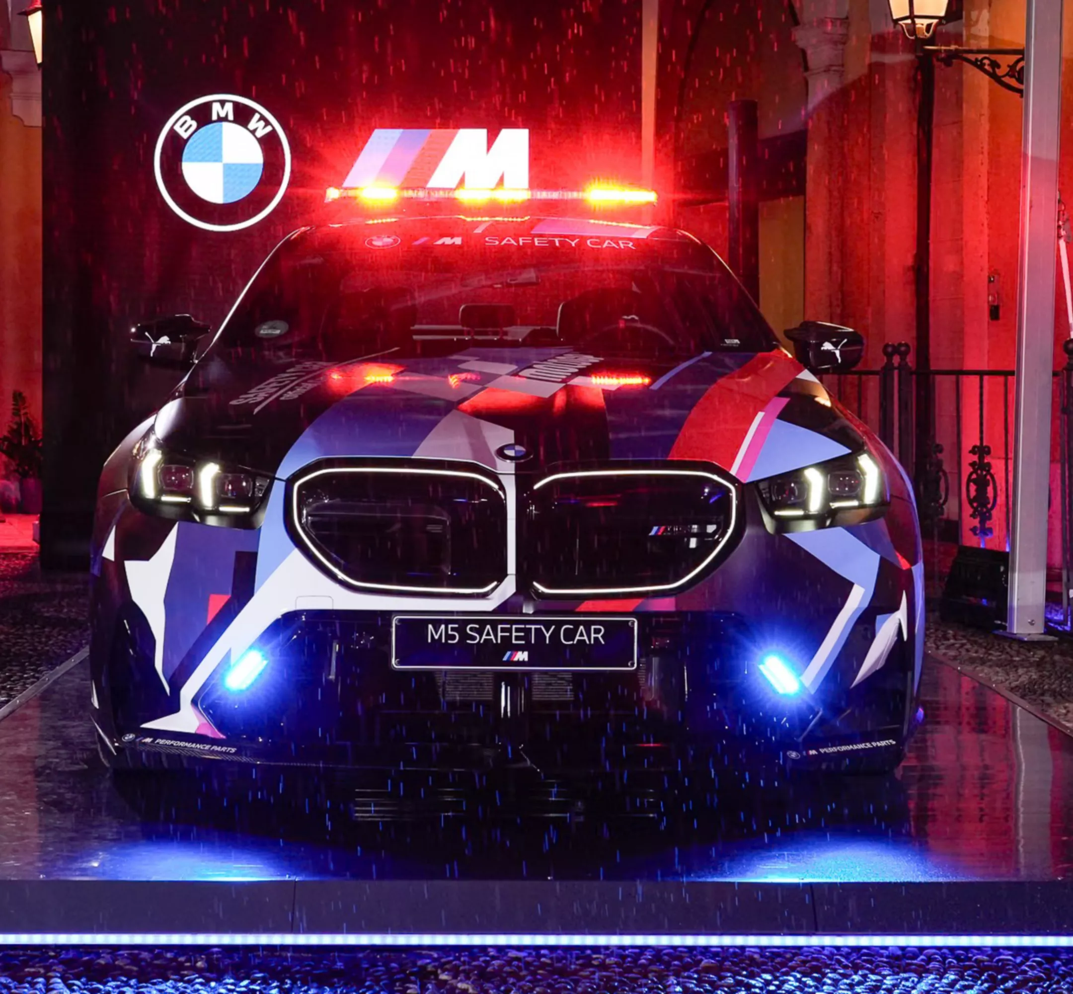 Ein roter sportlicher BMW fährt über eine Schotterstraße in einer grün bewachsenen Landschaft. 