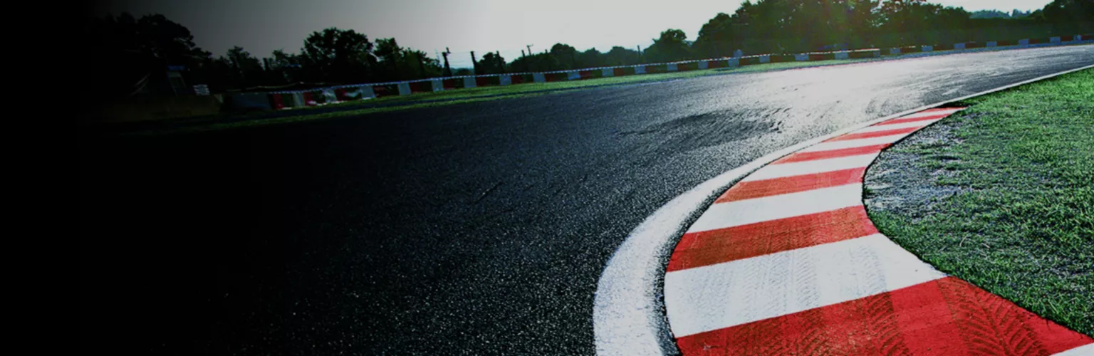 Close up of a racetrack, slightly slick with dew, with red and white striped curve hugging a tight corner of the track