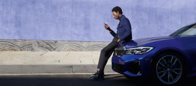 A man leans on the hood of his BMW as he uses his mobile phone.