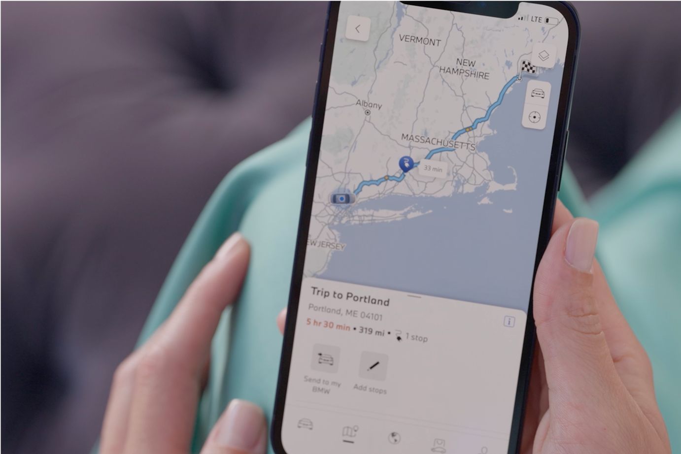 A hand holds a smartphone showcasing charging station locations on the My BMW App