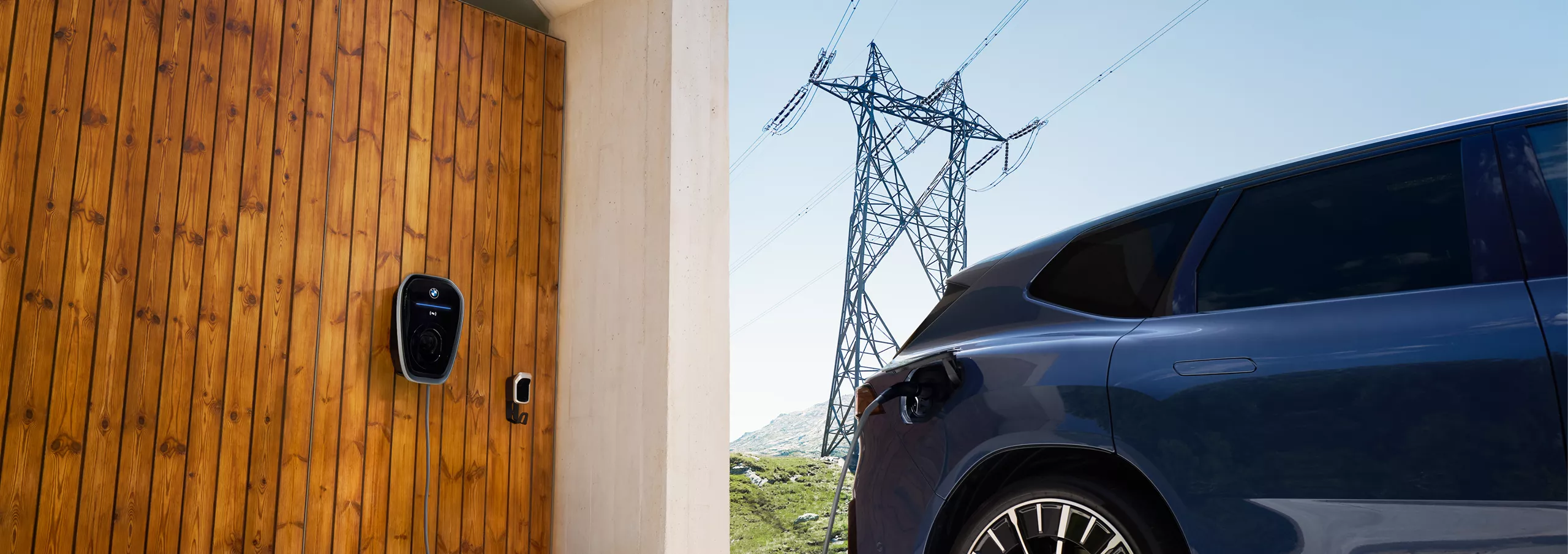 A BMW iX3 parked next to a BMW Wallbox with atransmission tower in the background 