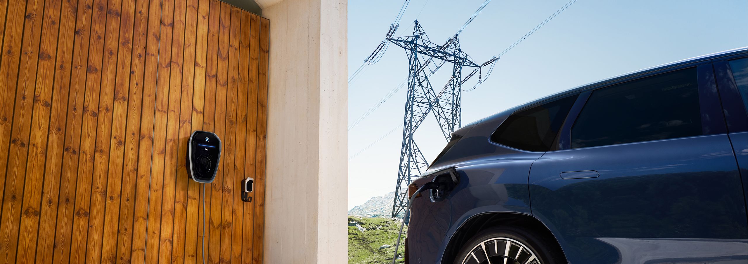 A BMW iX3 parked next to a BMW Wallbox with atransmission tower in the background 
