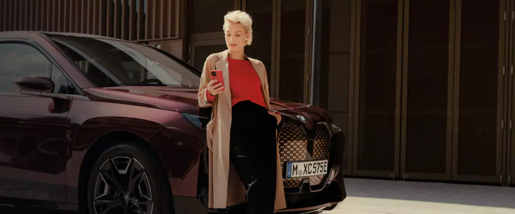 سيدة أمام السيارة BMW iX وتستخدم تطبيق My BMW app على الهاتف الذكي