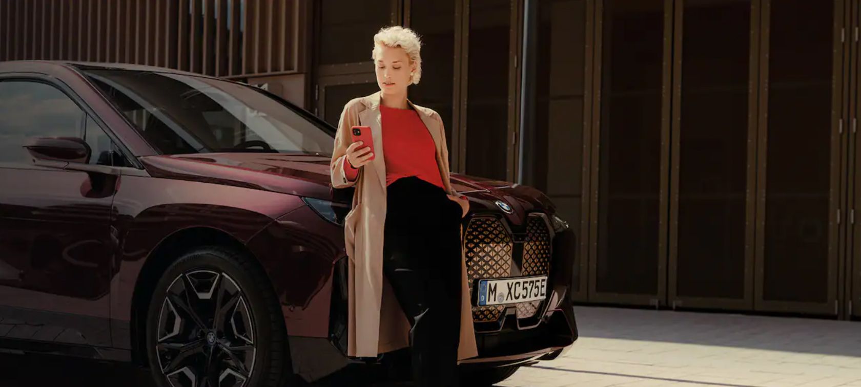  Woman in front of BWW iX uses My BMW app on smartphone