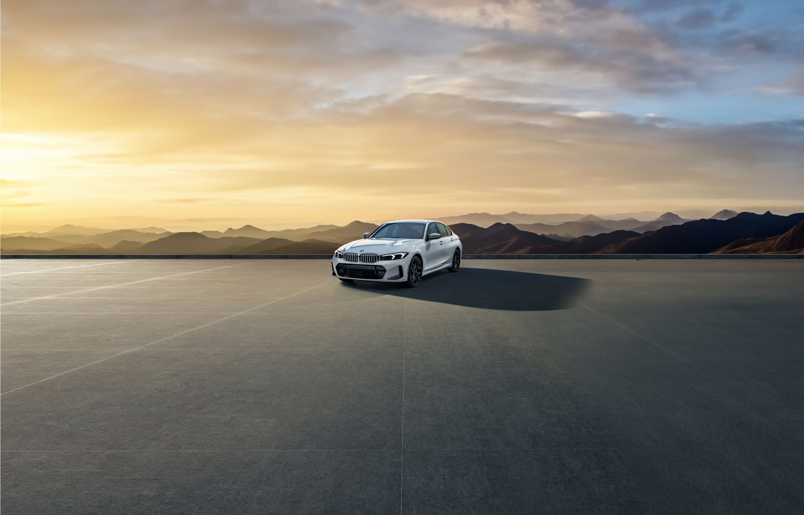 A BMW 3 Series parked on a concrete platform overlooking a shaded forest landscape at dusk