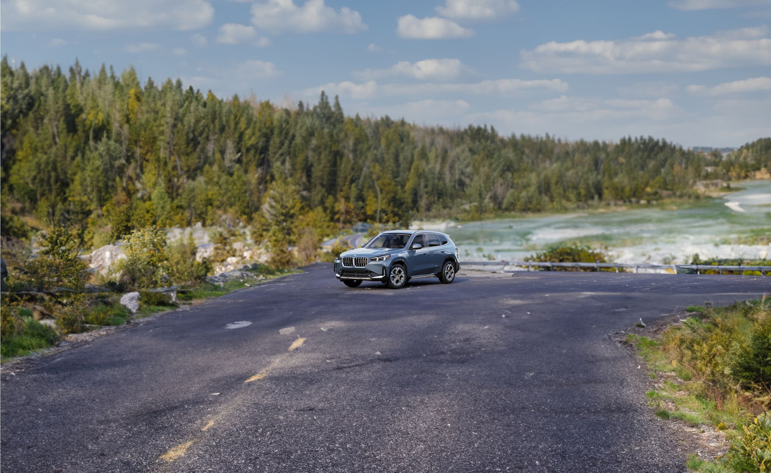 A BMW X1 parked on a mountain road with a rolling river in the background