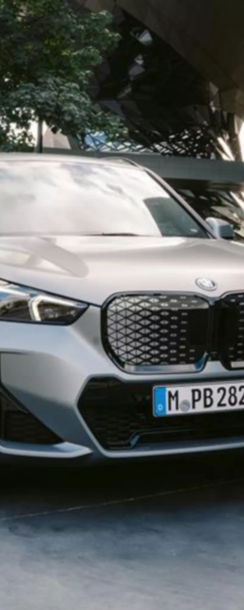 Η BMW iX1 παρκαρισμένη σε θέση με σήμανση δίπλα σε ένα μοντέρνο κτήριο, με ένα άτομο να περπατάει δίπλα.