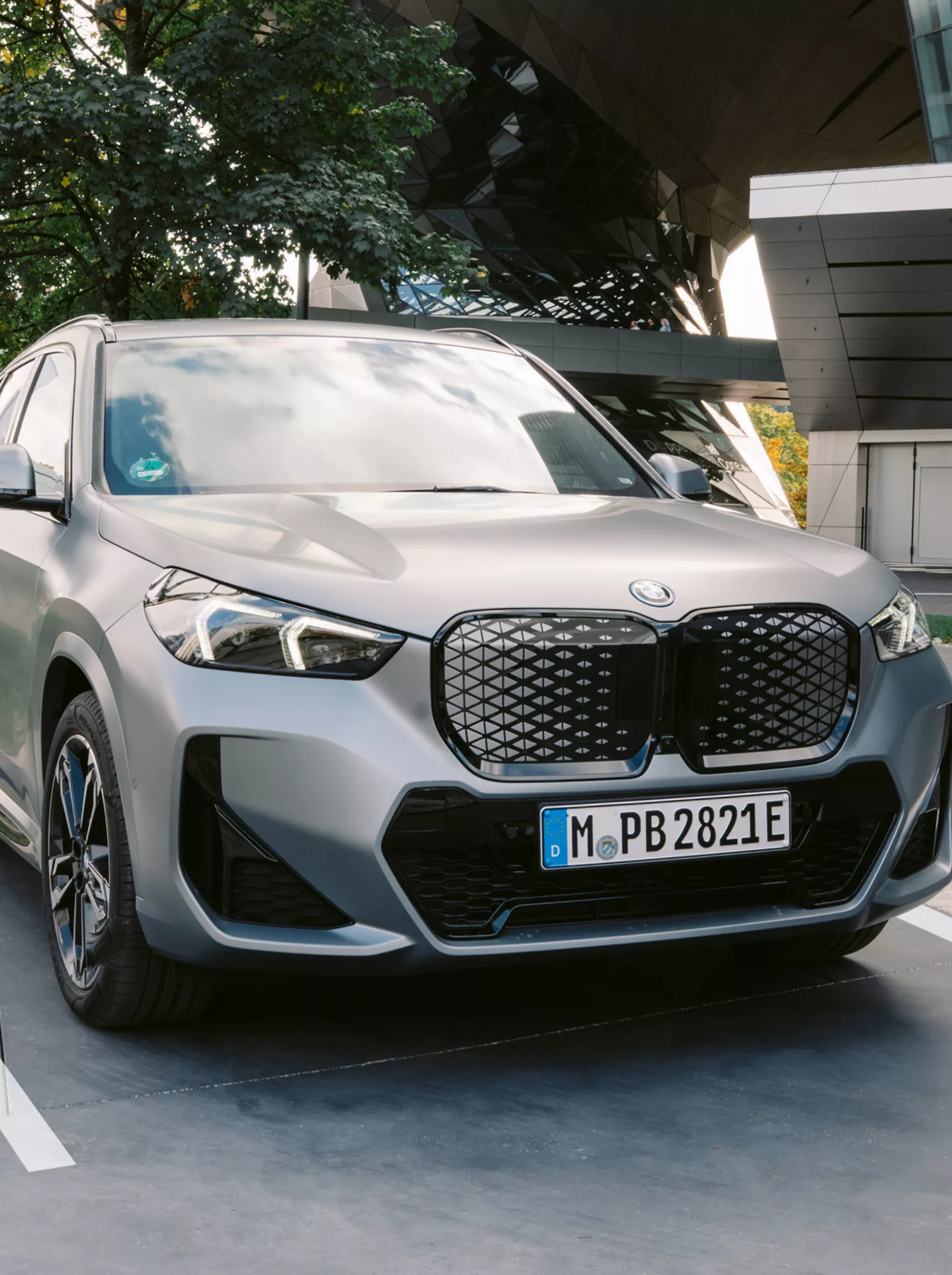 BMW iX1 aparcado en una plaza señalizada junto a un edificio moderno, con una persona cerca.