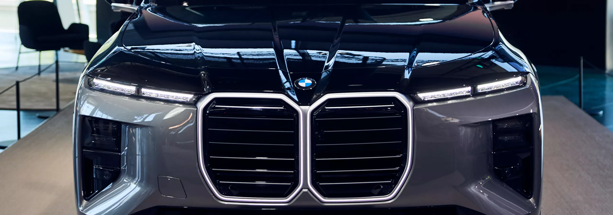 BMW 7er Limousine in Two‑Tone Lackierung Oxidgrau und Saphirschwarz, ausgestellt in der BMW Welt vor moderner Glasarchitektur.
