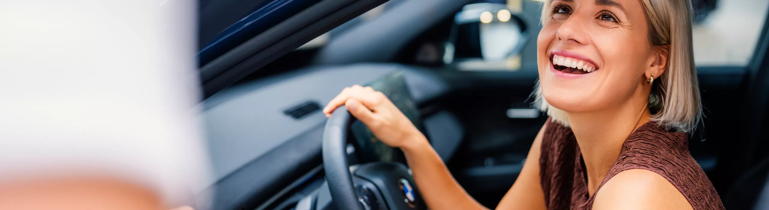 Eine erwachsene Frau sitzt im BMW iX3, dessen Vordertür offen steht.