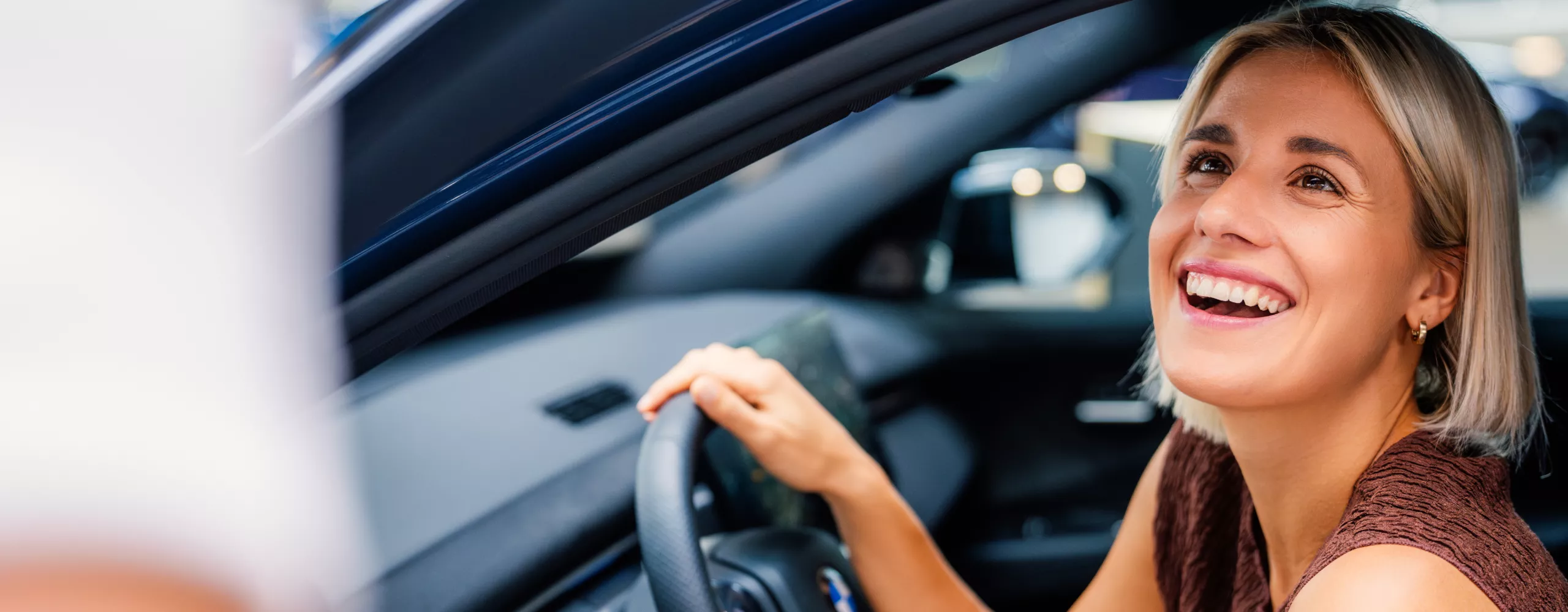 An adult woman sitting in the BMW iX3 with the front door open. 