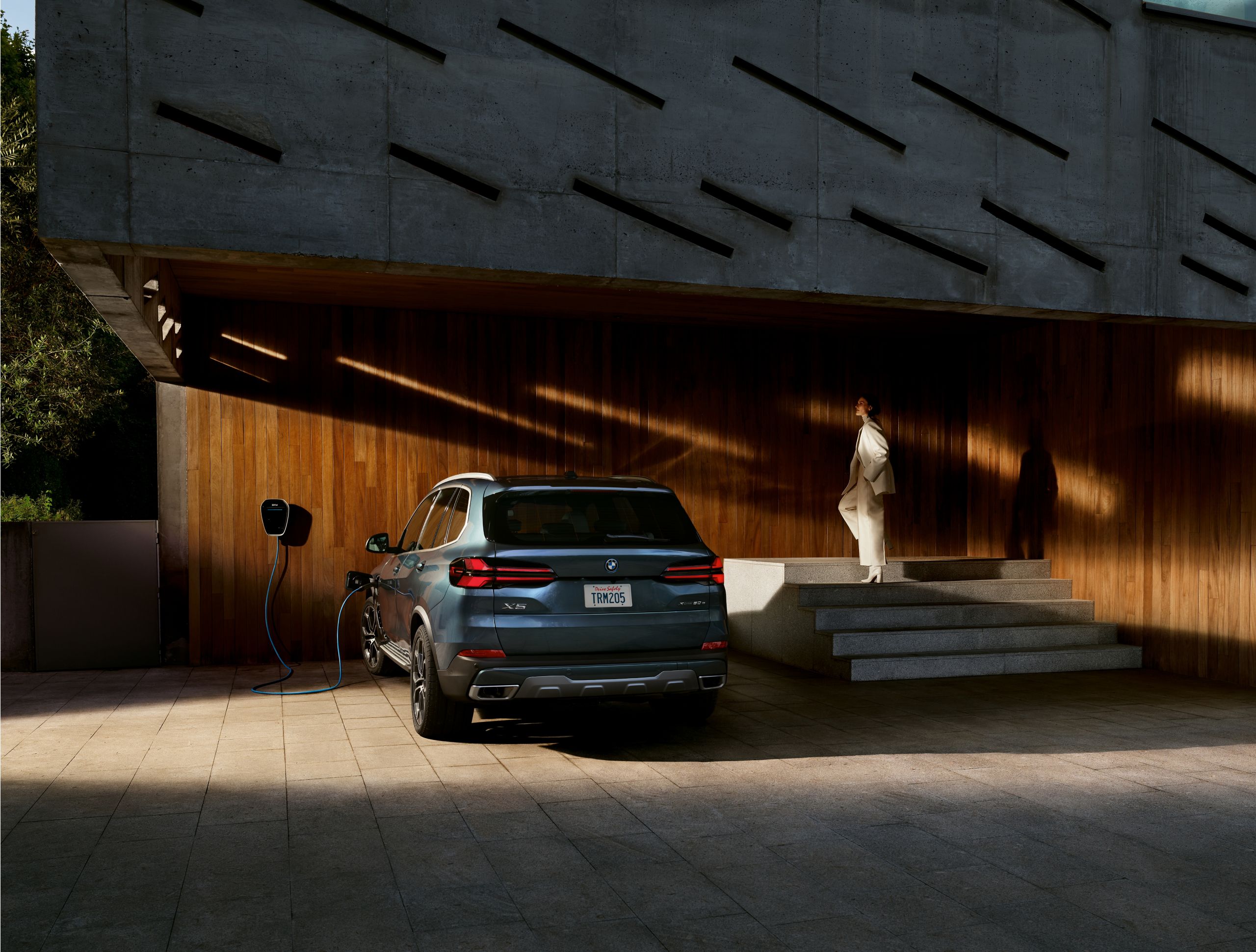 A driver stands near her BMW X5 xDrive50w as it charges with a BMW Wallbox outside her home
