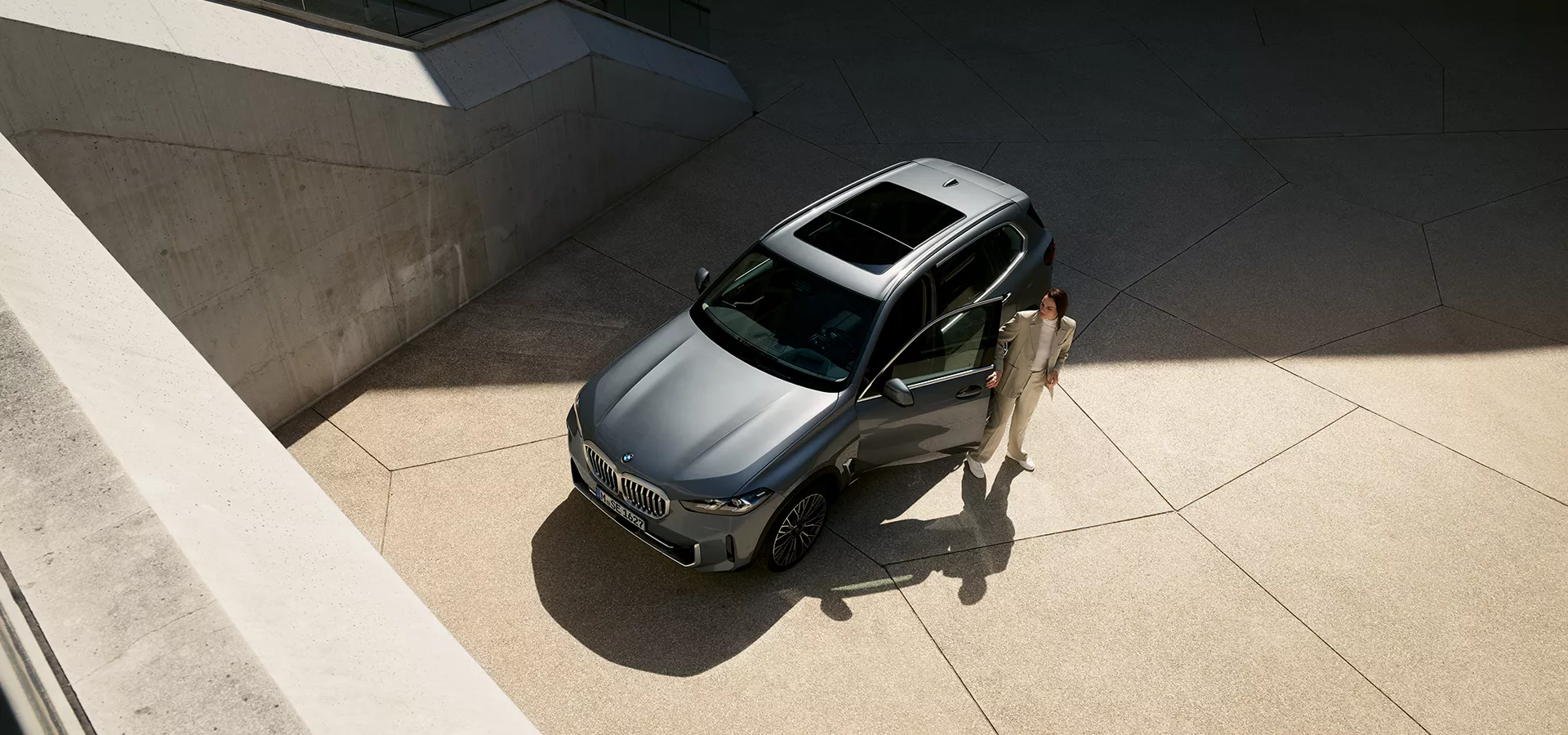 Vogelperspektive einer aus einem grauen BMW X5 aussteigenden Frau.