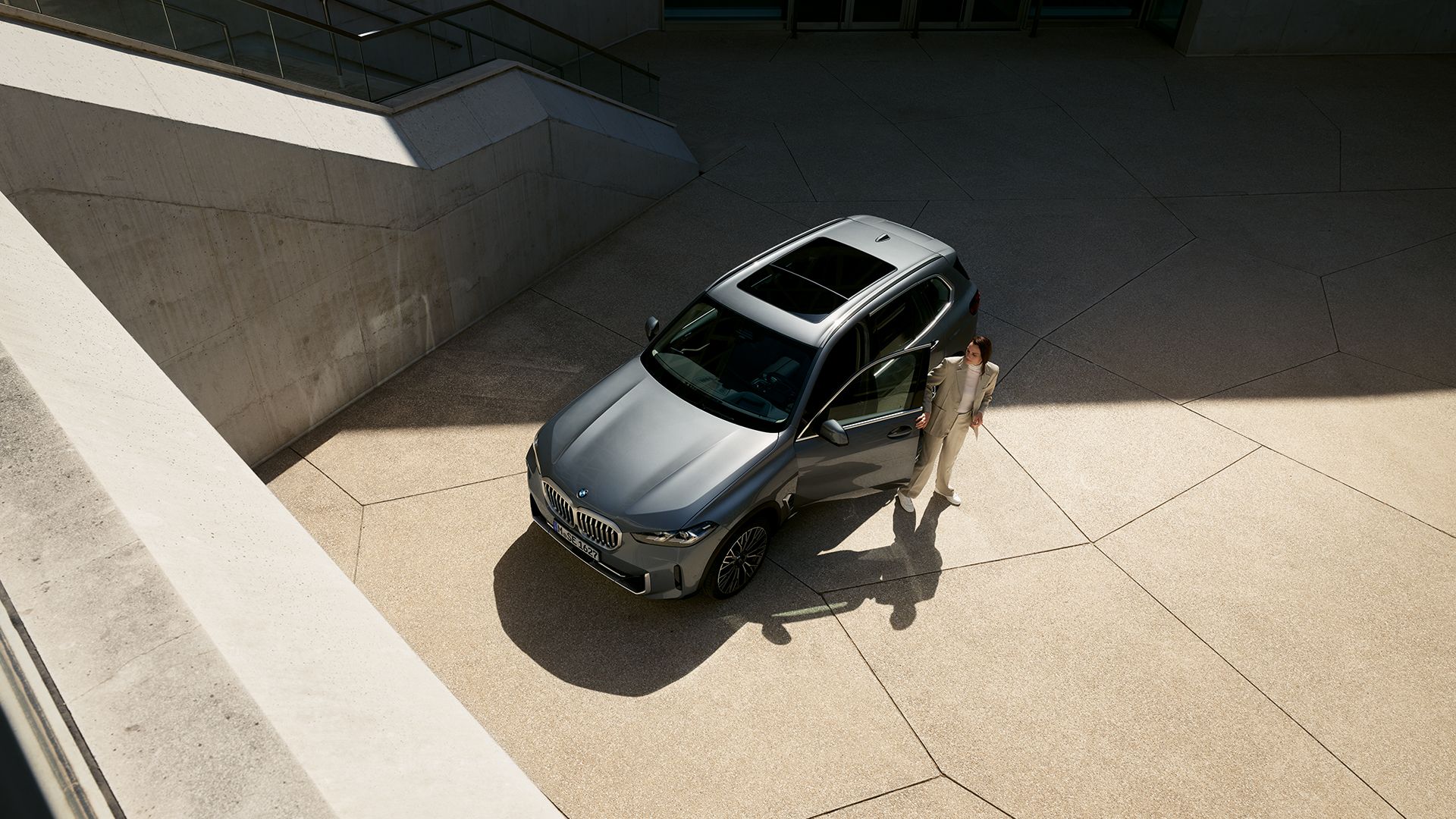 Vogelperspektive einer aus einem grauen BMW X5 aussteigenden Frau.