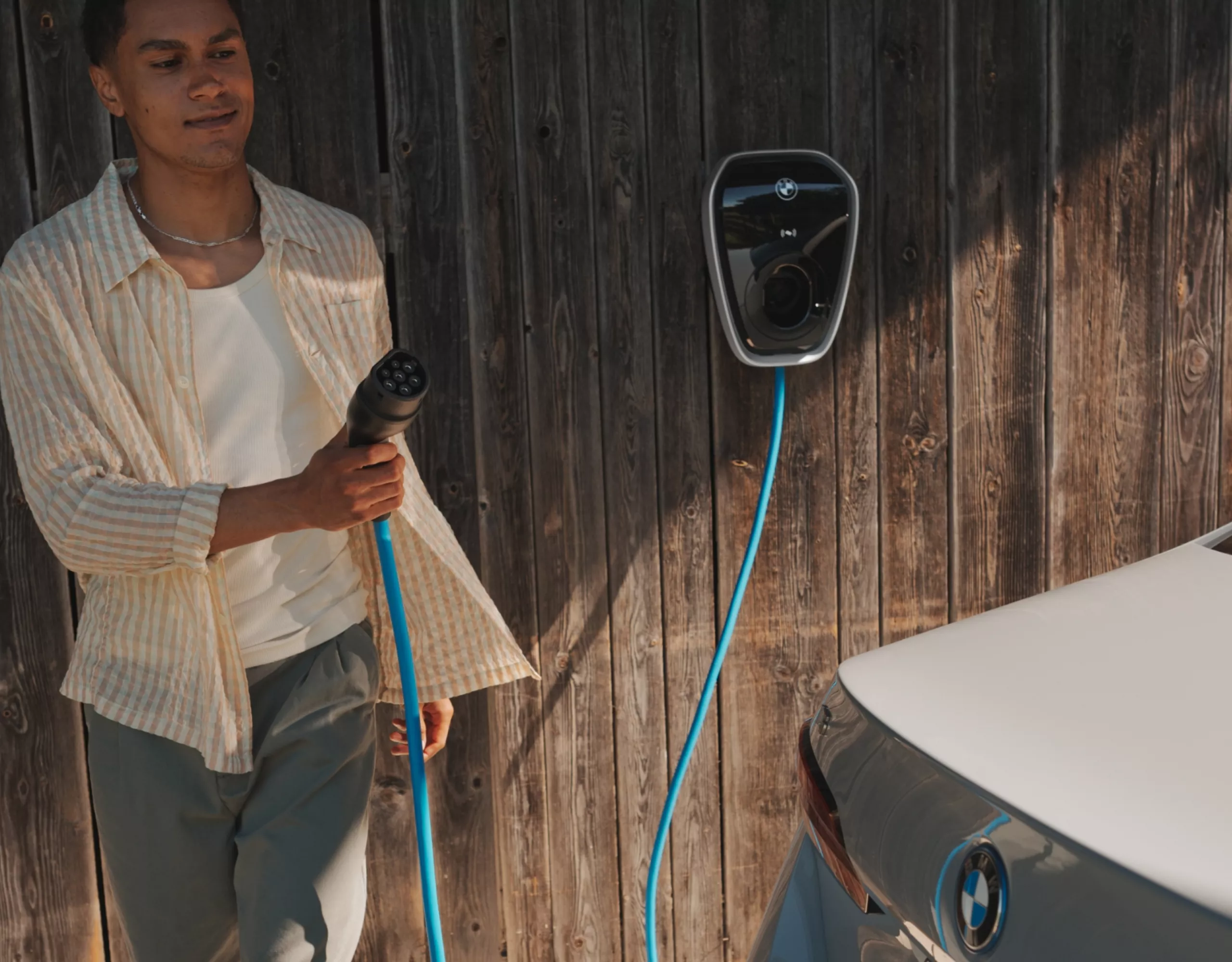 Person mit Ladekabel einer Wallbox geht zu einem BMW